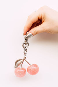 Pink cherry-shaped keychain held by a hand on a white background