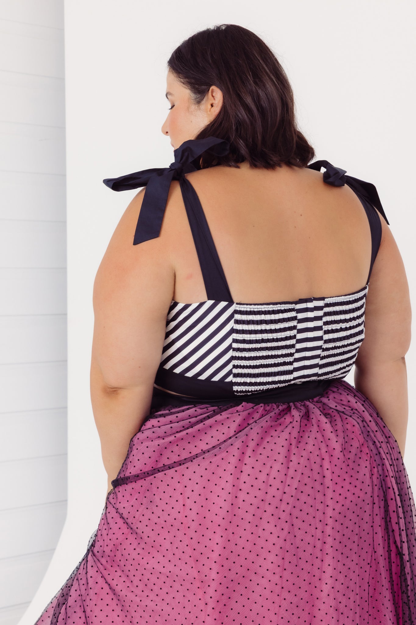 Back view of a plus woman wearing a Cherry Bobbins cotton black and white striped top with a pink tulle skirt on a white background