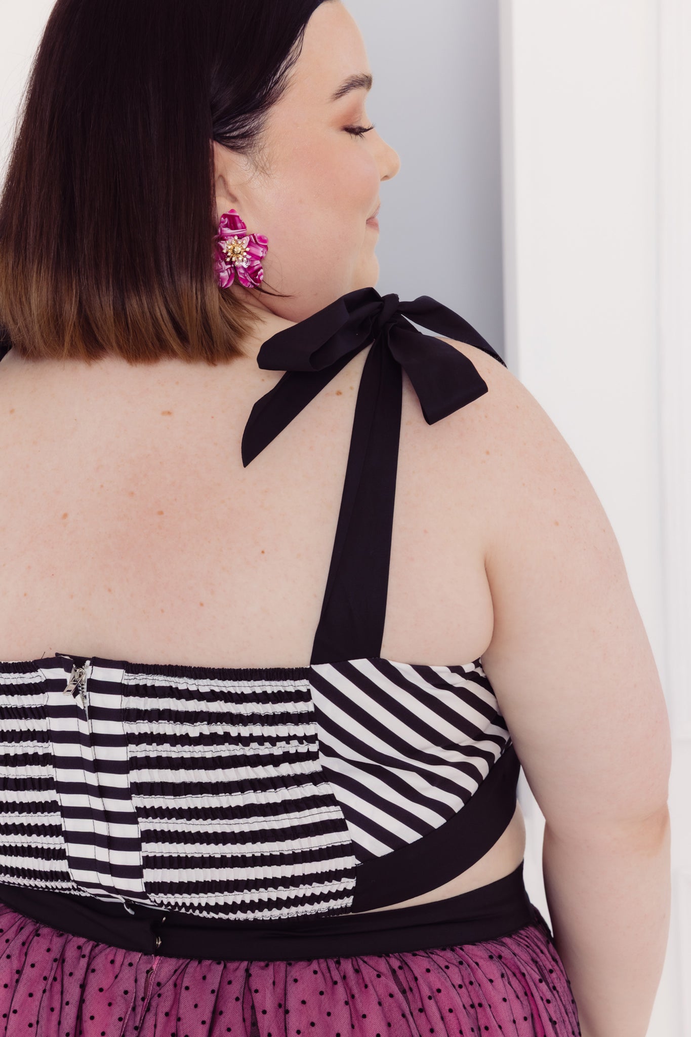 Woman wearing a Cherry Bobbins size inclusive black and white striped top with a bow detail on a plain background