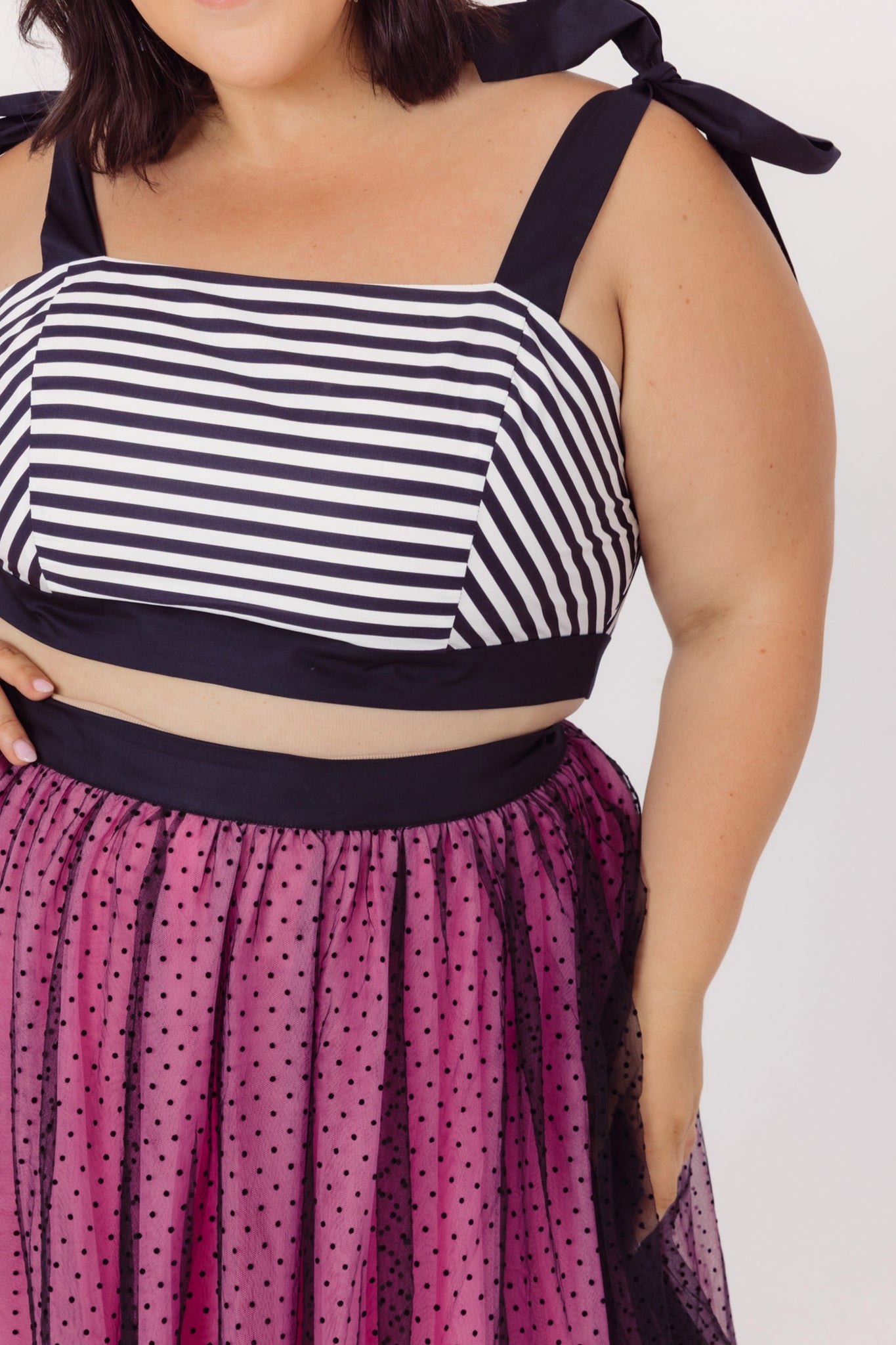 Close up of outfits details of plus size woman wearing a Cherry Bobbins cotton striped top and polka dot tulle skirt on a white background