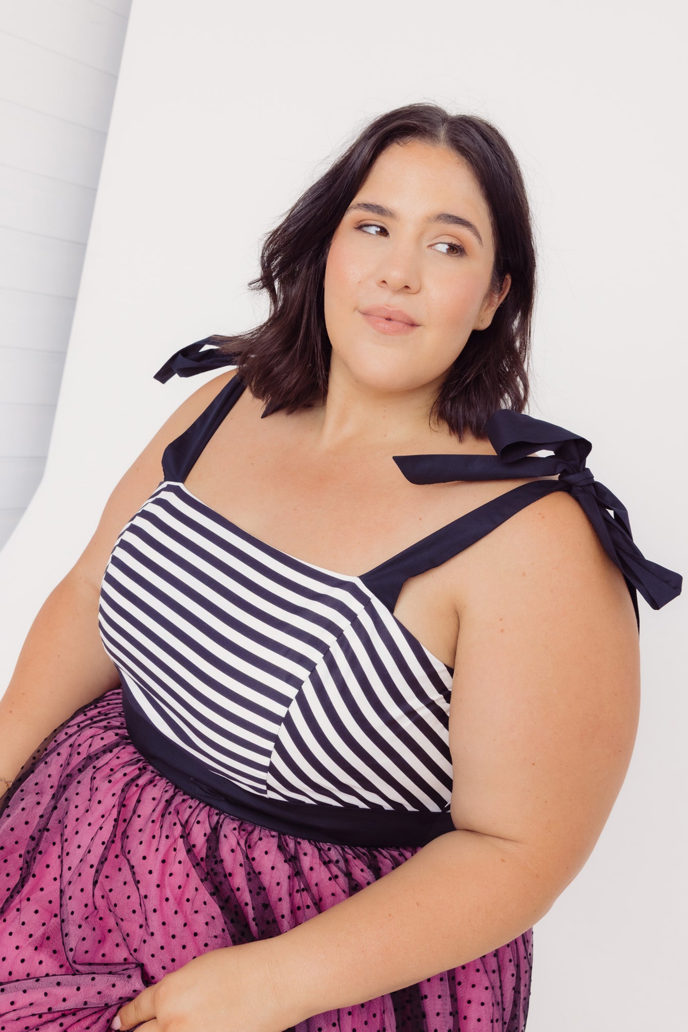 Woman sitting wearing a Cherry Bobbins black and white striped top with a pink polka dot tulle skirt on a white background