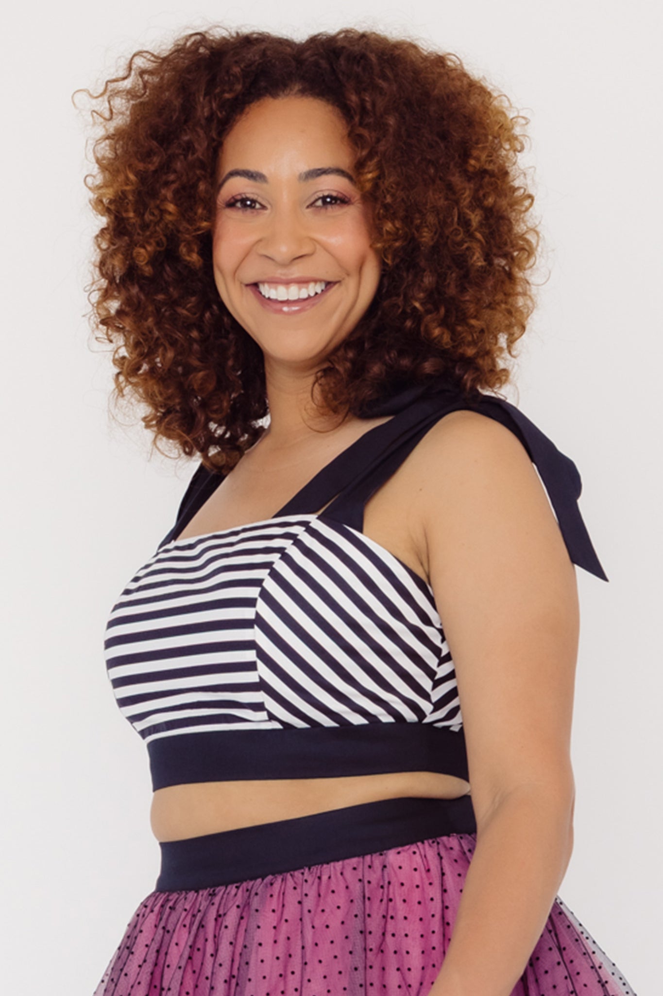 Close up side view of a woman wearing a Cherry bobbins striped cotton top and pink tulle skirt with a white background