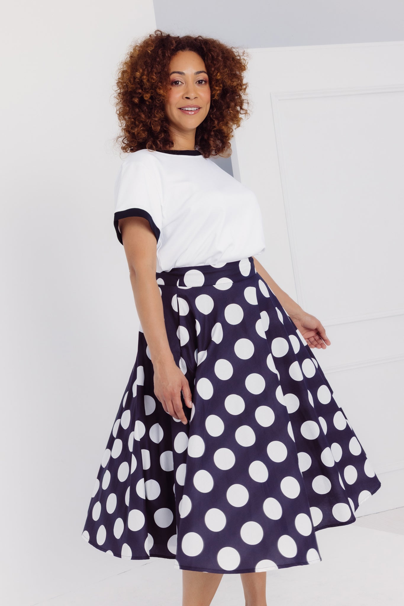 Close up view of a woman wearing a Cherry Bobbins white tee and black skirt with white polka dots on a plain background
