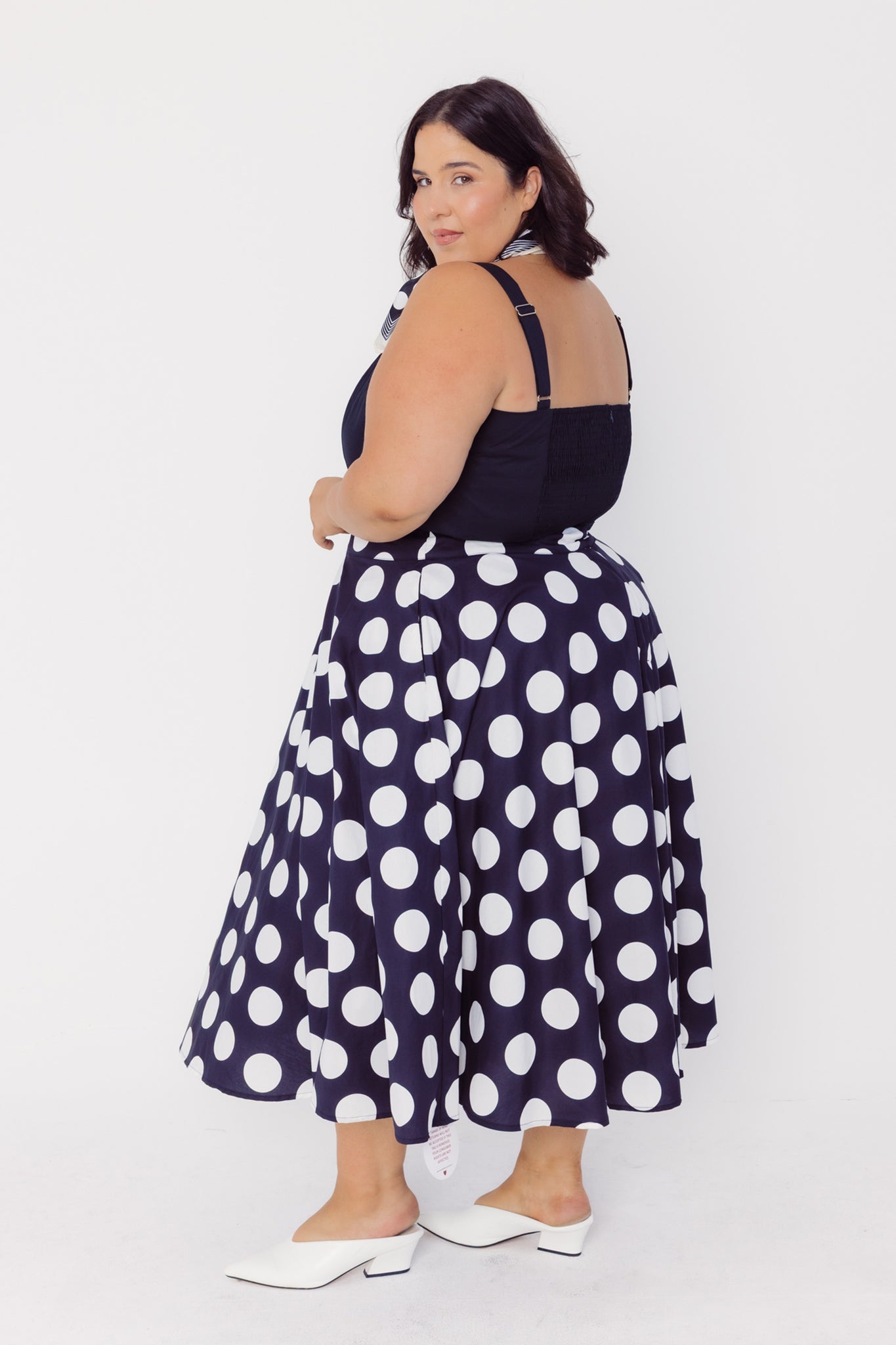 Back side view of a woman wearing a Cherry Bobbins black skirt with white polka dots on a white background