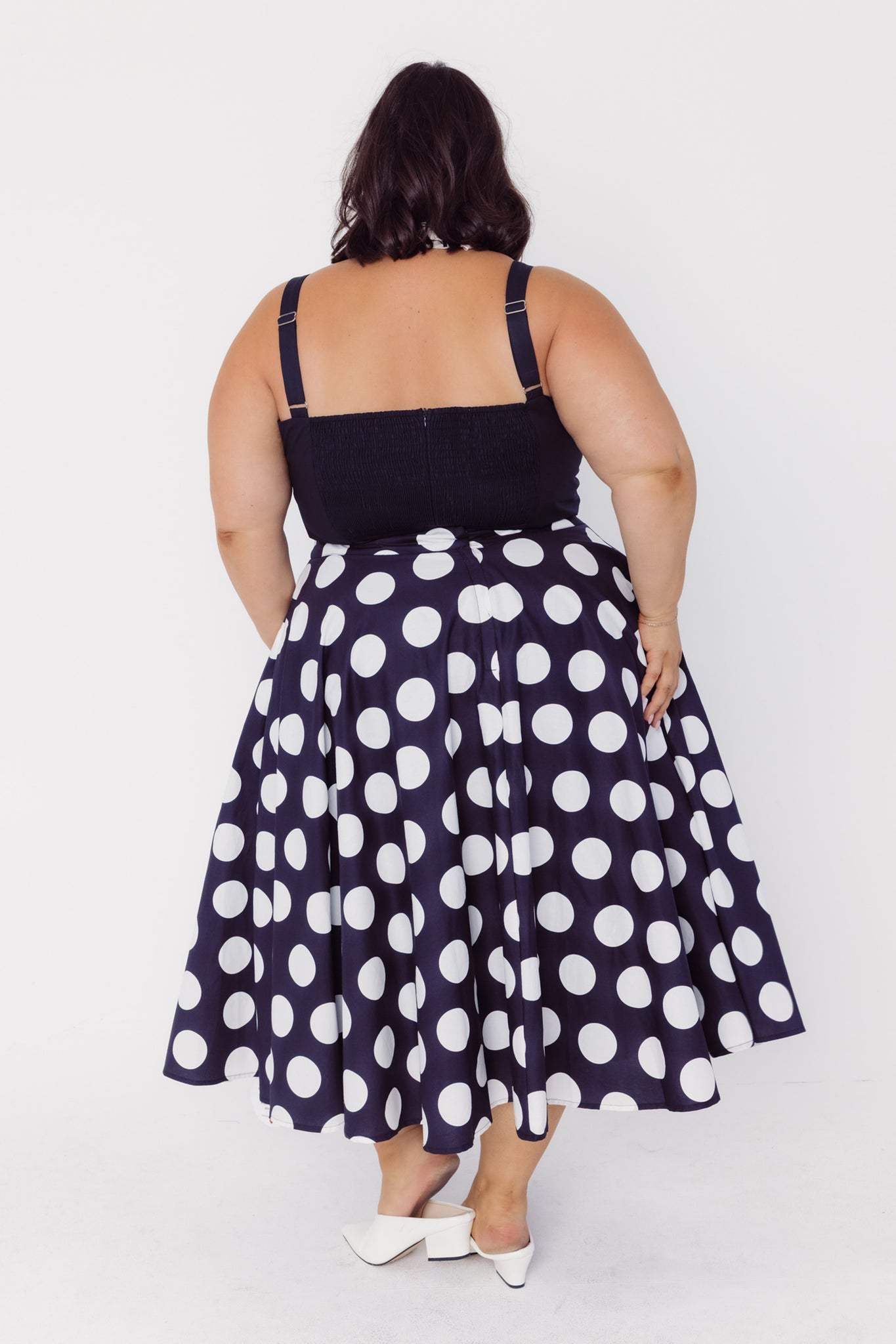 Back view of a woman wearing a Cherry Bobbins black top and polka dot cotton circle skirt on a white background