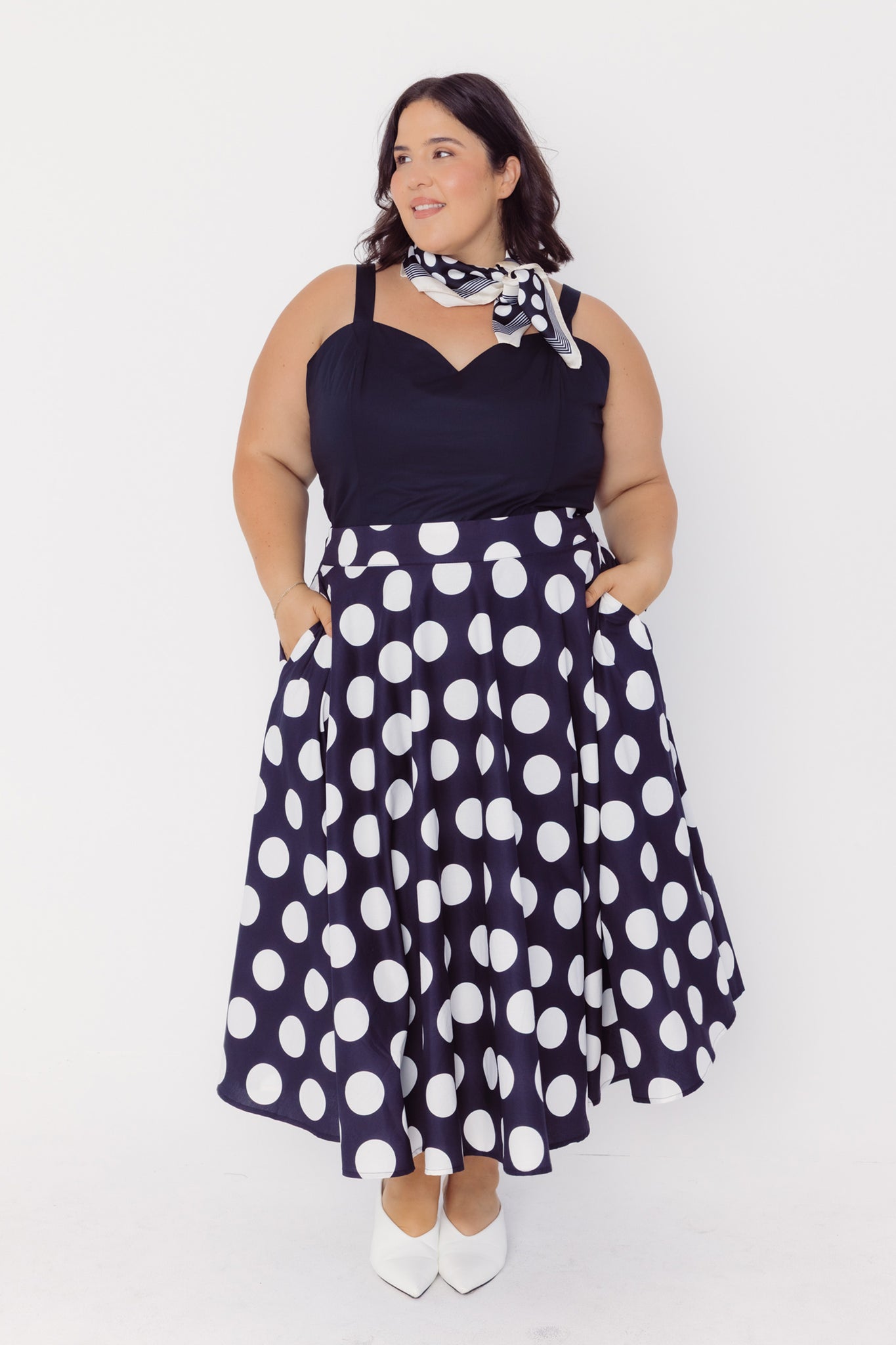 Front view of a woman wearing a Cherry Bobbins black top and polka dot cotton skirt with a white background