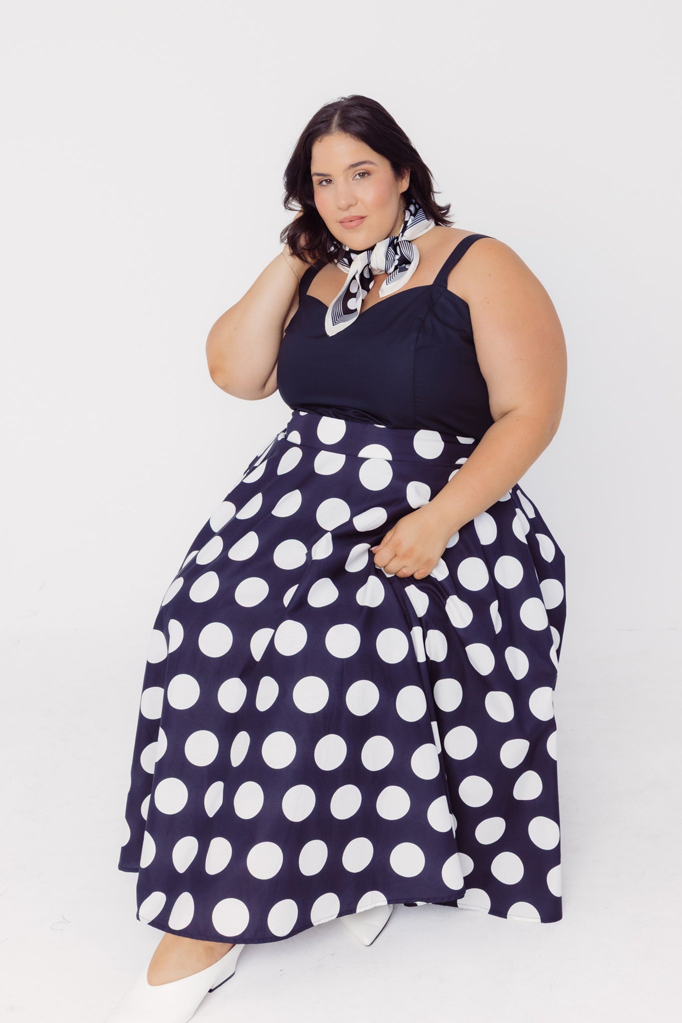 Woman sitting wearing a Cherry Bobbins black polka dot cotton skirt and black top on a white background