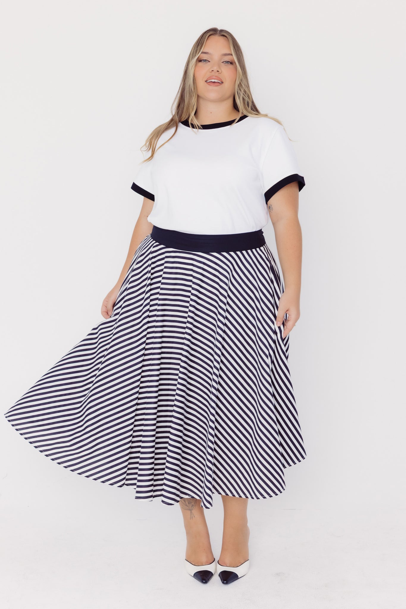Front view of a woman wearing a Cherry Bobbins white tee with black trim and a black and white striped cotton circle skirt on a white background