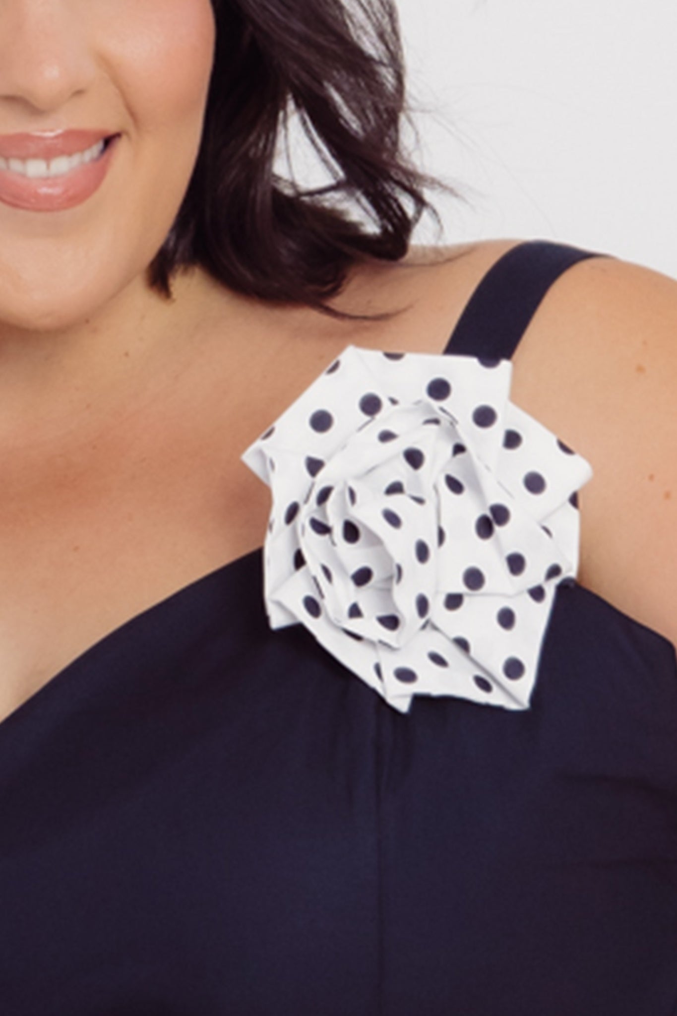Black cotton dress with a white polka dot flower rose brooch on a plain background
