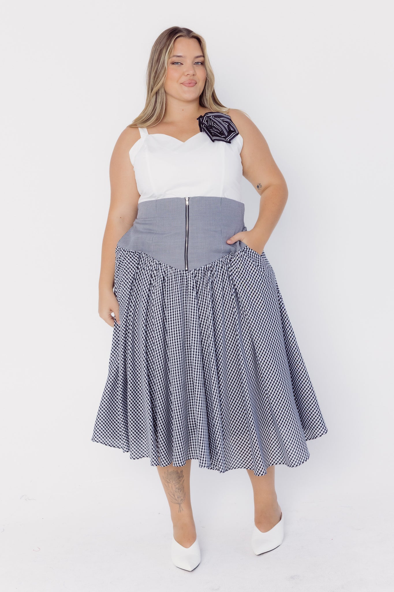 Woman wearing a white top with a rose striped cotton brooch and black checkered skirt on a white background