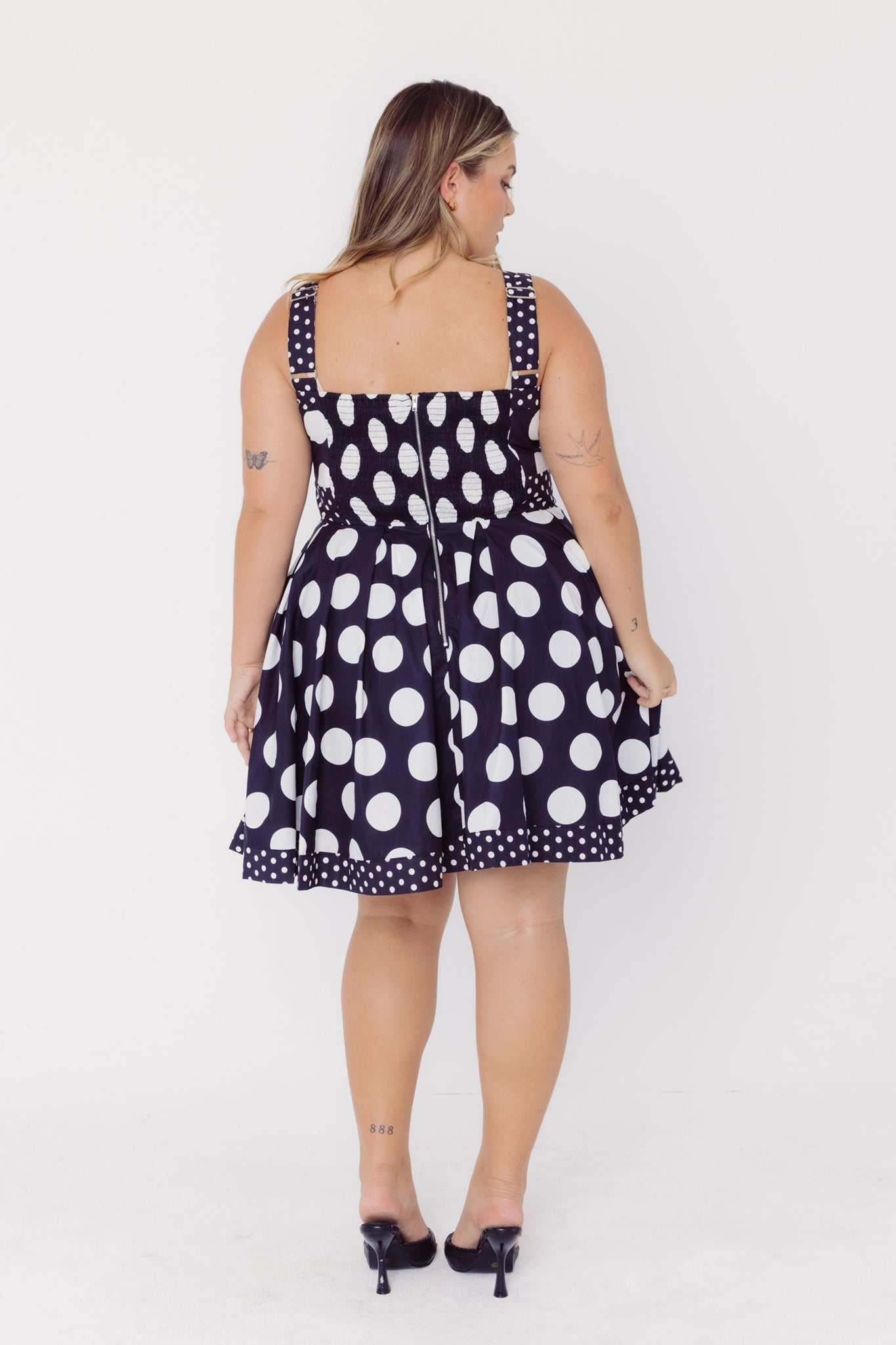 Back view of a woman wearing a Cherry Bobbins black mid-size cotton polka dot dress on a white background