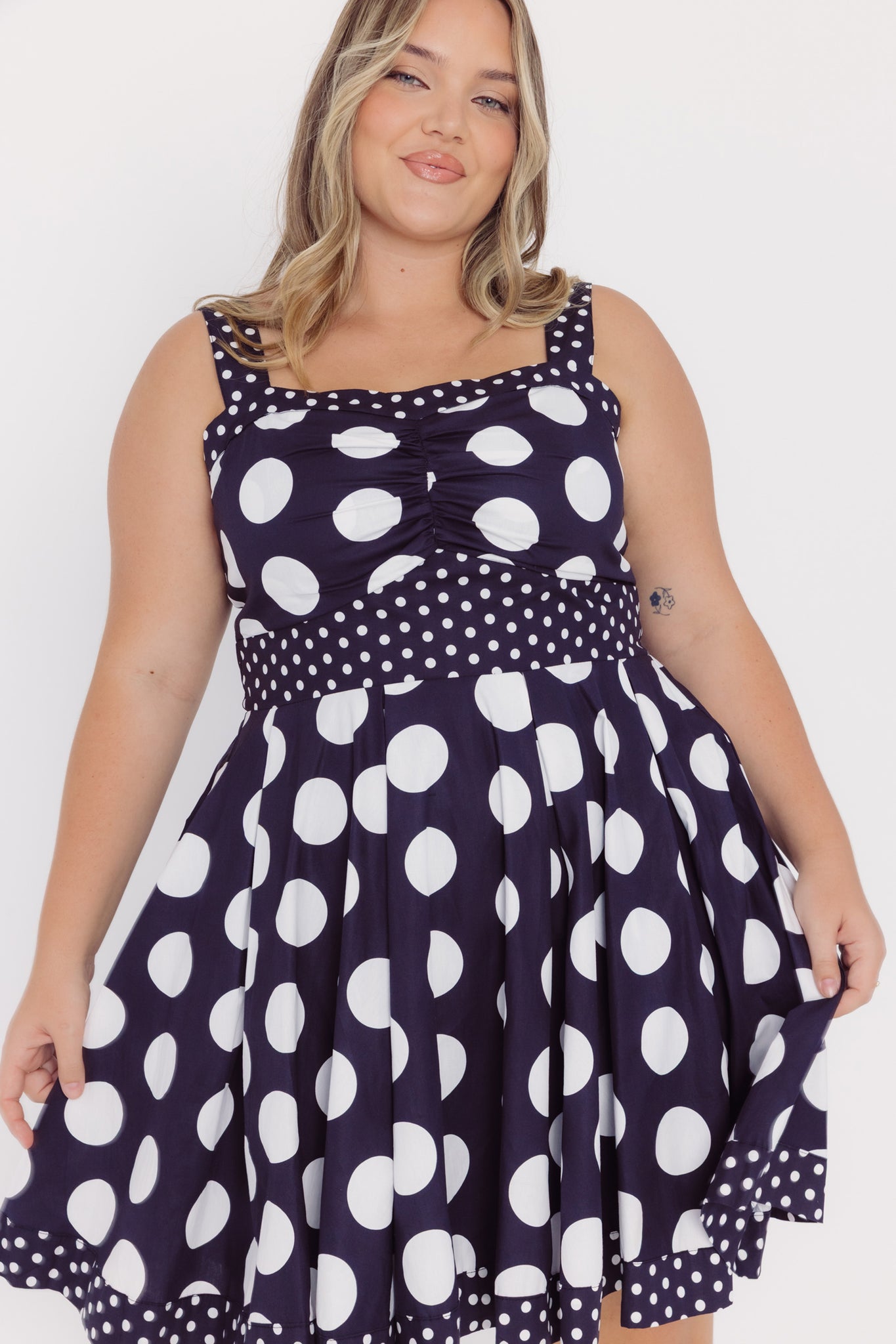 Close-up view of a woman wearing a Cherry Bobbins black cotton mid-size dress with white polka dots on a white background
