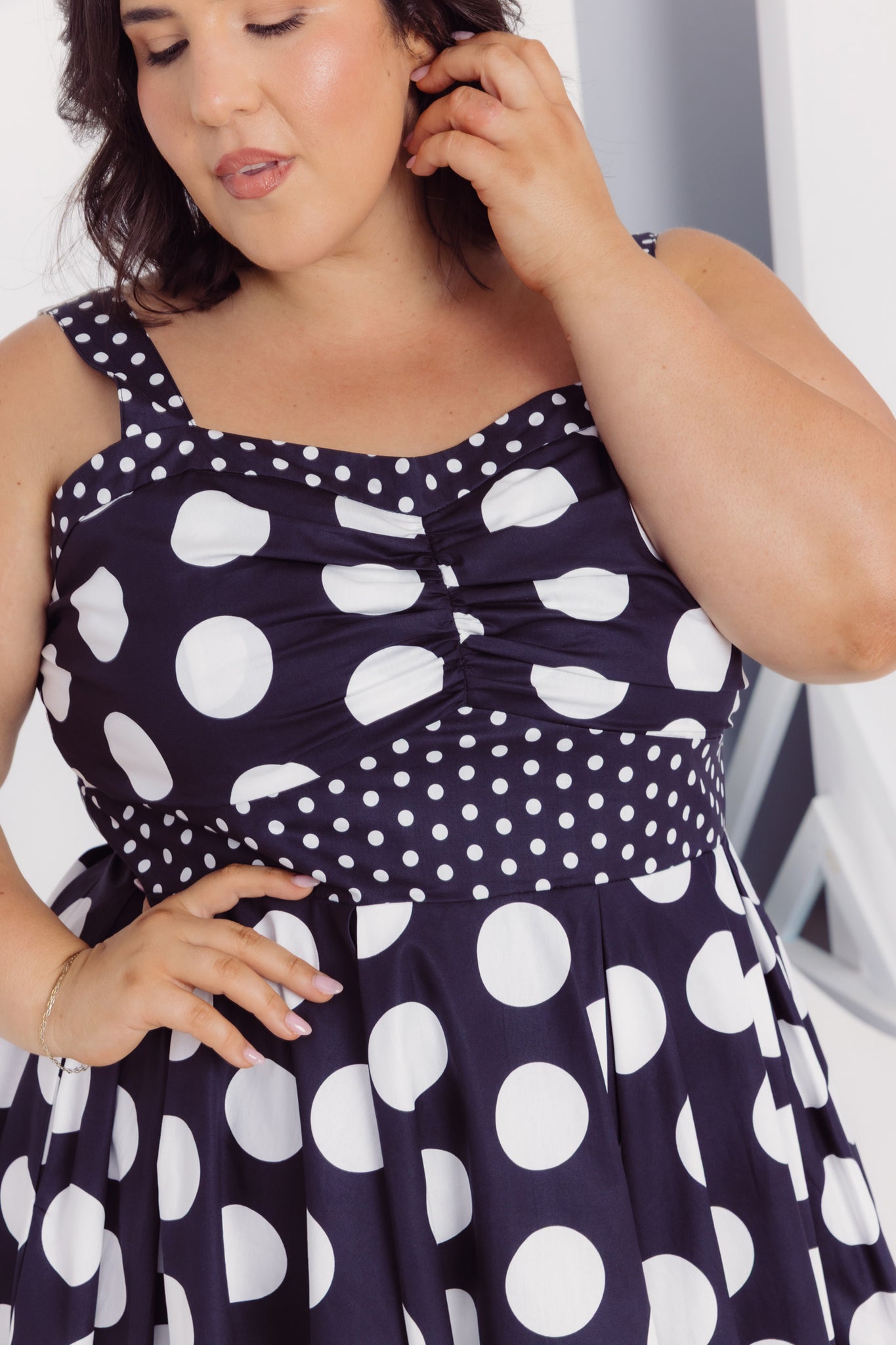 Close-up view of a woman wearing a Cherry Bobbins black cotton plus size dress with white polka dots, adjusting her hair.