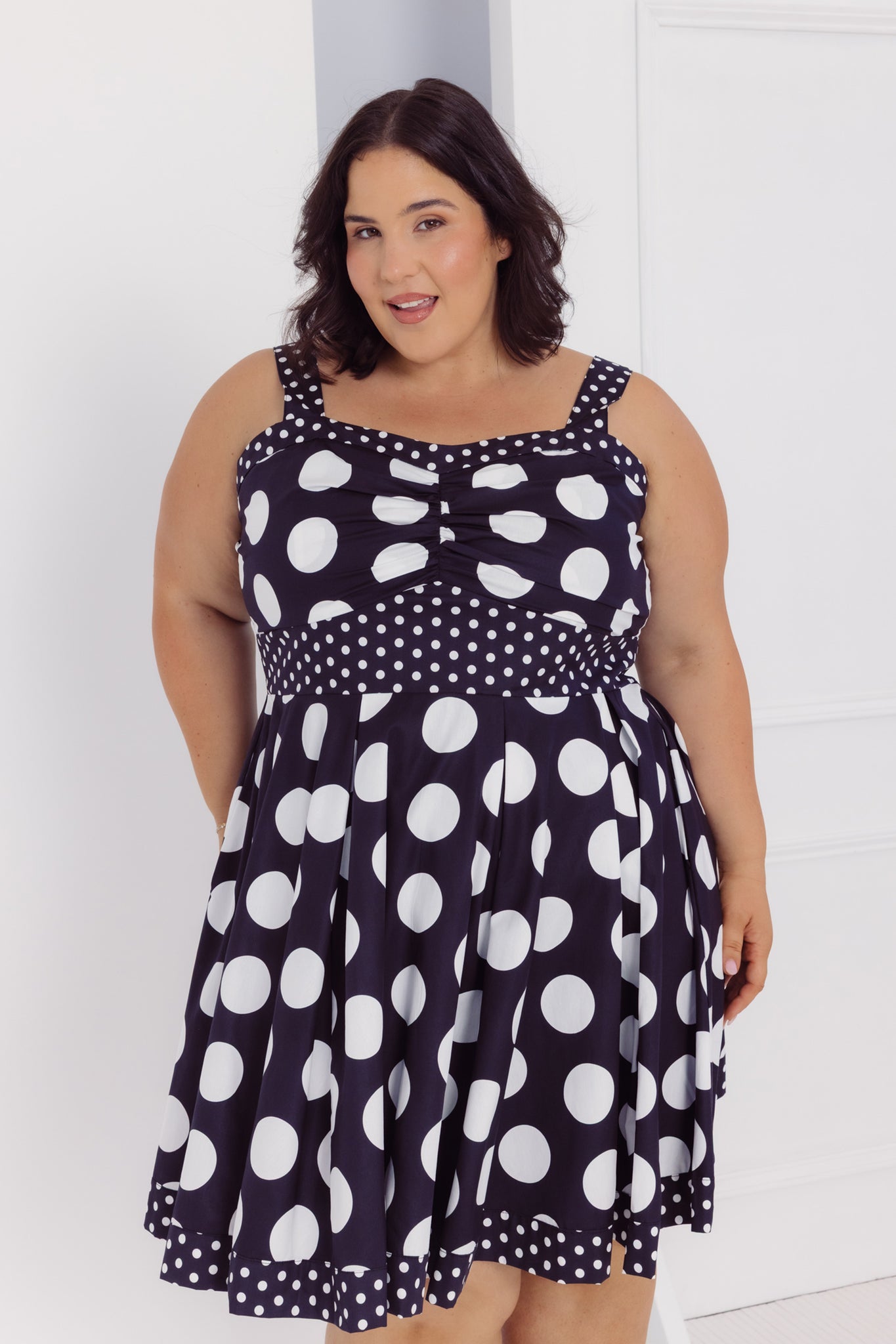 Front view of a woman wearing a Cherry bobbins black cotton plus size dress with white polka dots against a white background