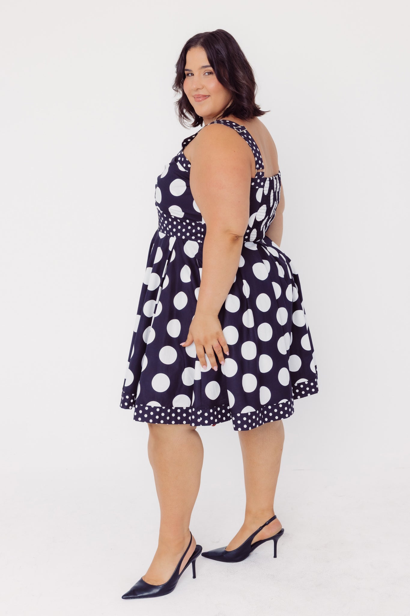 Side view of a woman wearing a Cherry bobbins cotton plus size polka dot dress on a white background