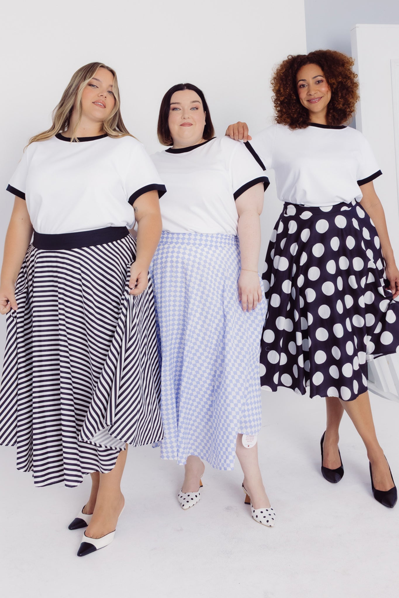 Three women wearing Cherry Bobbins white cotton blend t-shirts and patterned skirts on a white background