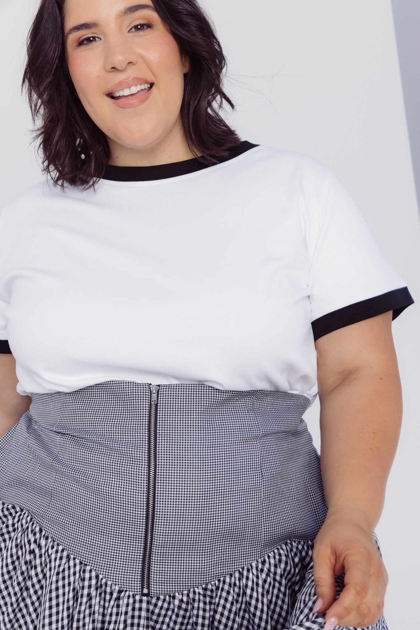 Smiling woman wearing a Cherry Bobbins white cotton blend t-shirt with black trim and a checkered skirt 