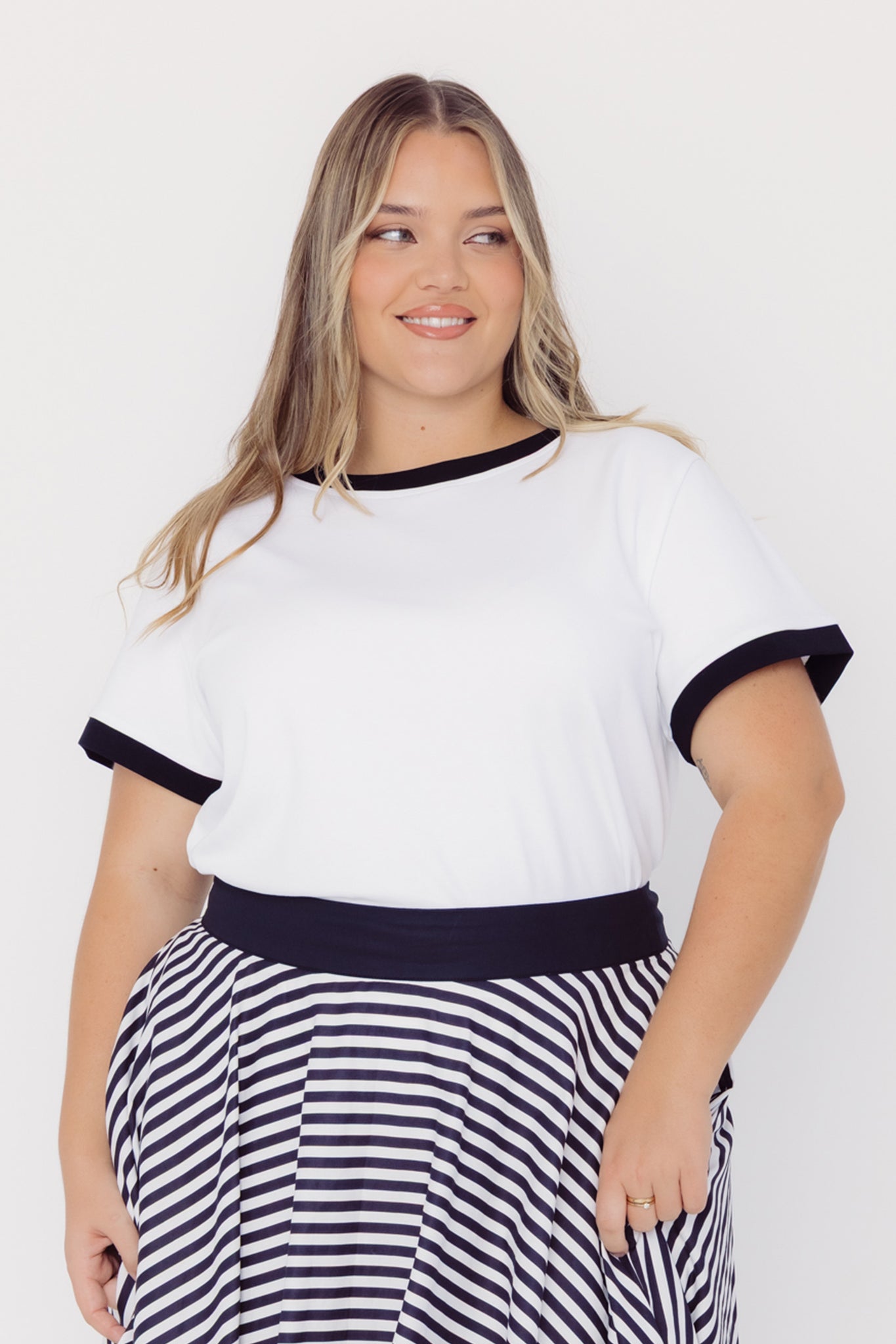 Front view of a woman wearing a Cherry Bobbins cotton blend white top with black trim and a striped skirt on a white background
