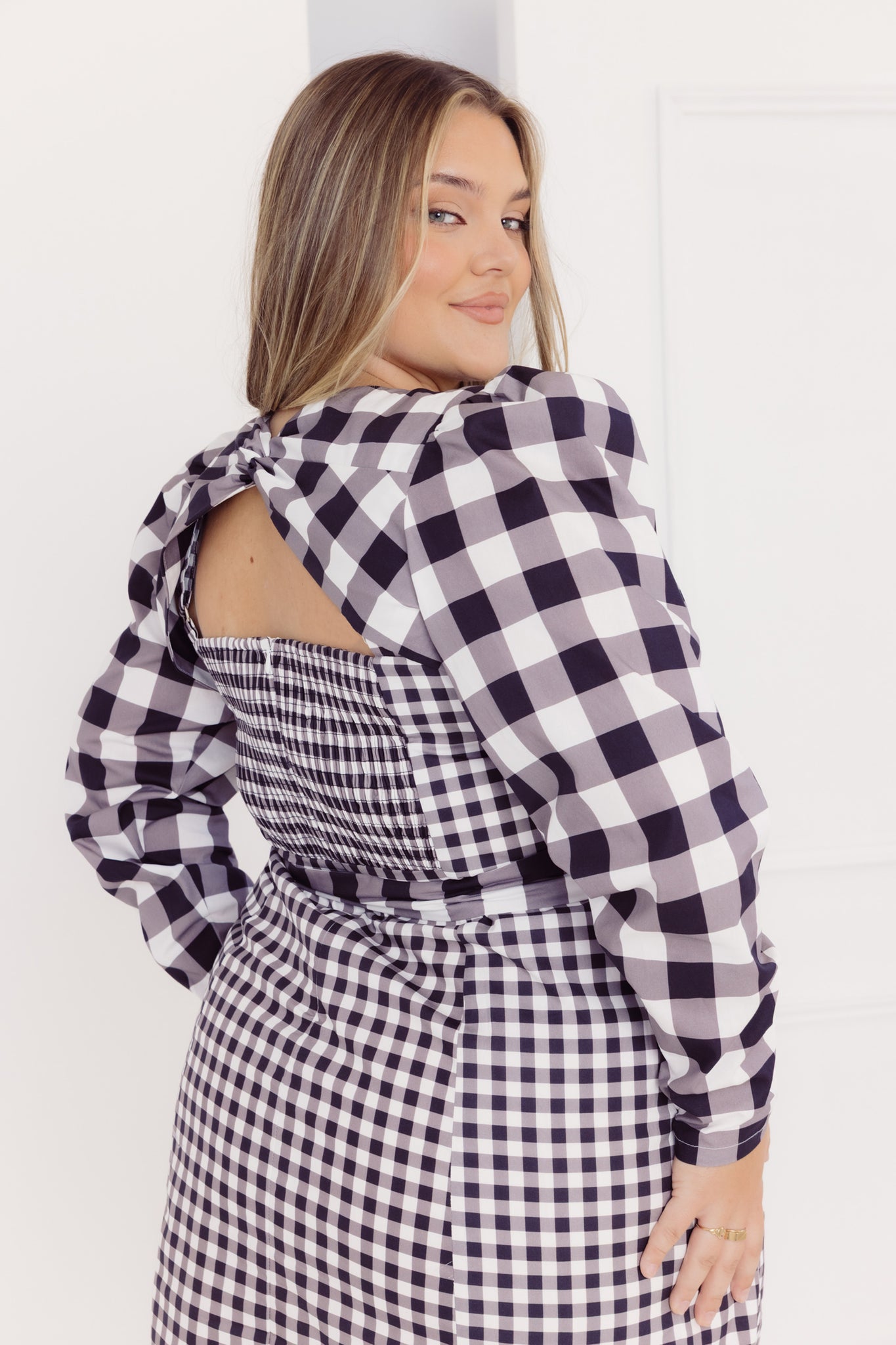 Back view of a woman wearing a black and white Cherry Bobbins checkered dress with long sleeves against a white background