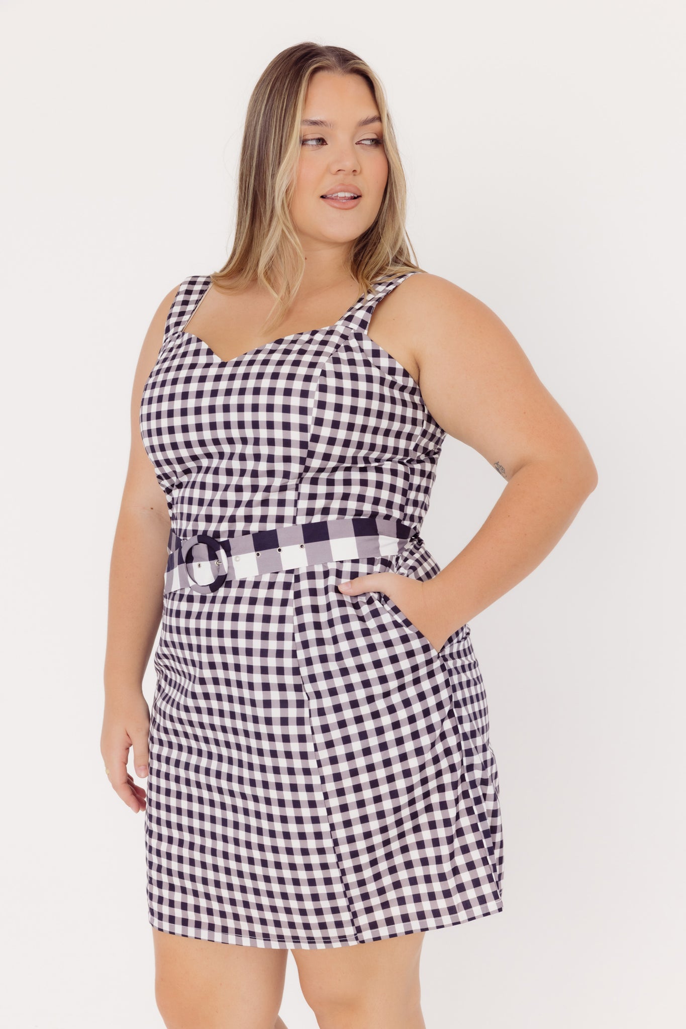 Close-up view of a woman wearing a black and white checkered dress with contrasting belt on a white background
