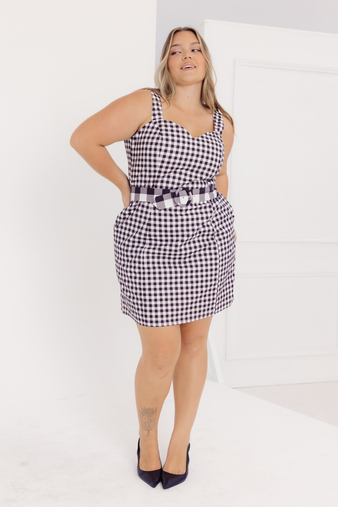 Front view of a woman wearing a black and white Cherry Bobbins checkered dress with a belt against a white background