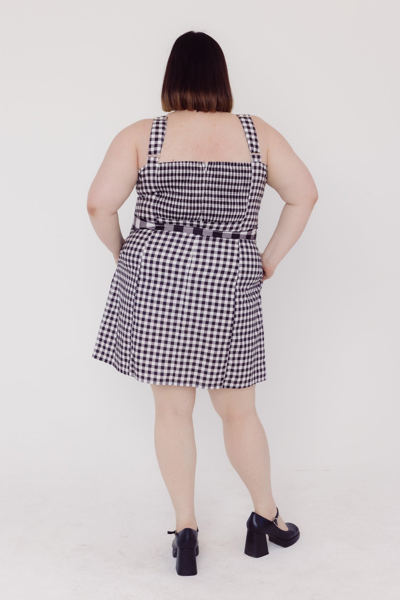 Back view of a woman wearing a black and white Cherry Bobbins checkered plus size dress on a white background