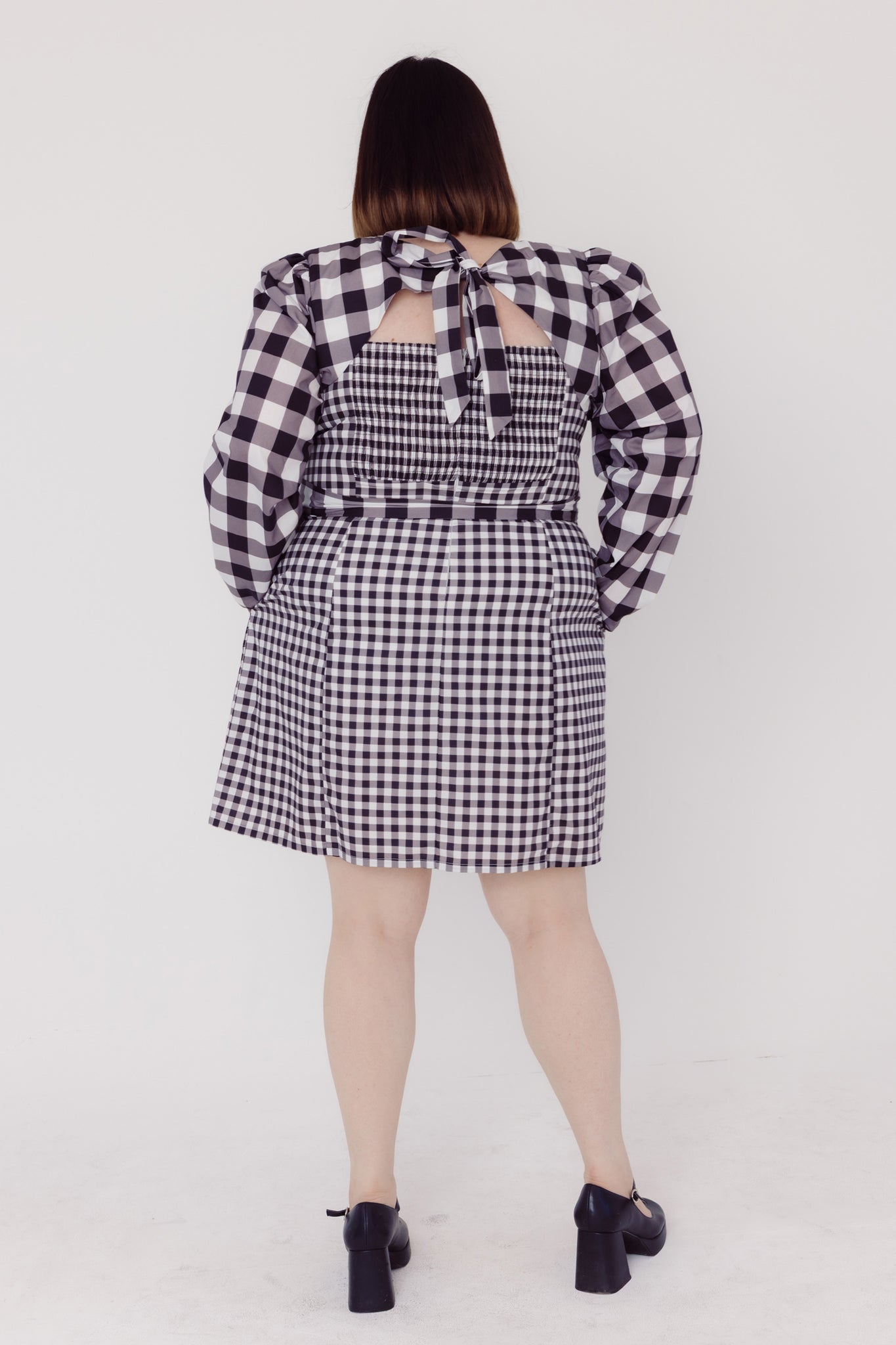 Back view of a woman wearing a black and white Cherry Bobbins checkered plus size dress with a bolero on a white background