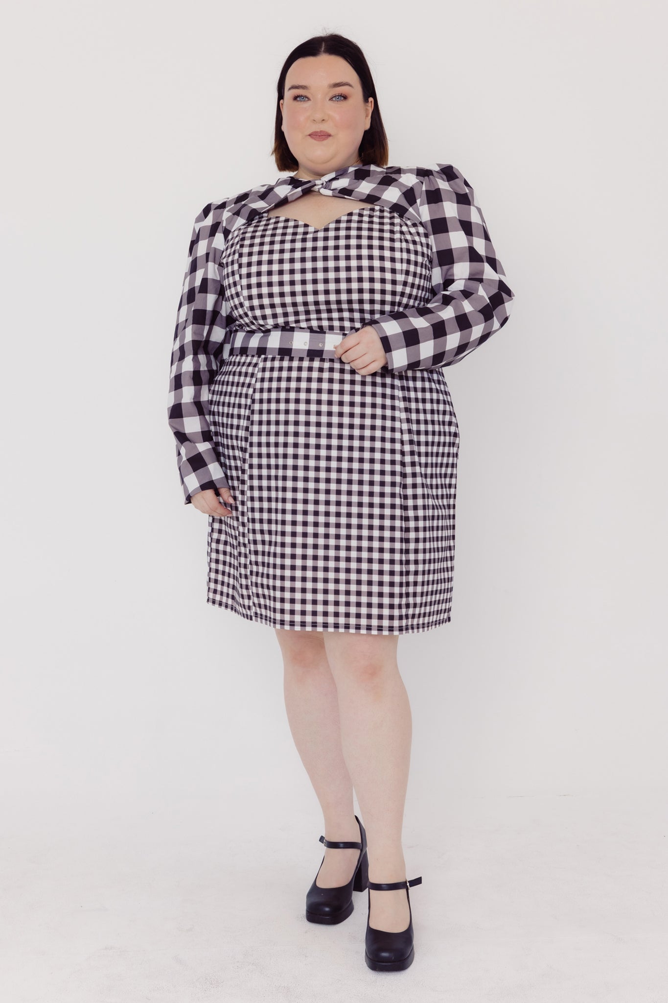 Front view of a woman wearing a black and white Cherry Bobbins checkered plus size dress on a white background