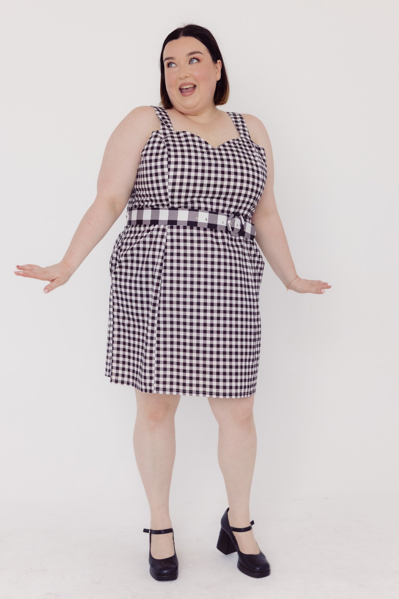 Front view of a woman wearing a black and white Cherry Bobbins checkered plus size dress with a belt on a white background