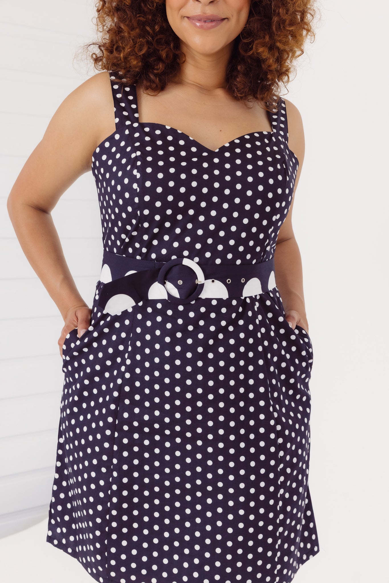 Close up view of a woman wearing a black Cherry Bobbins polka dot dress a white background