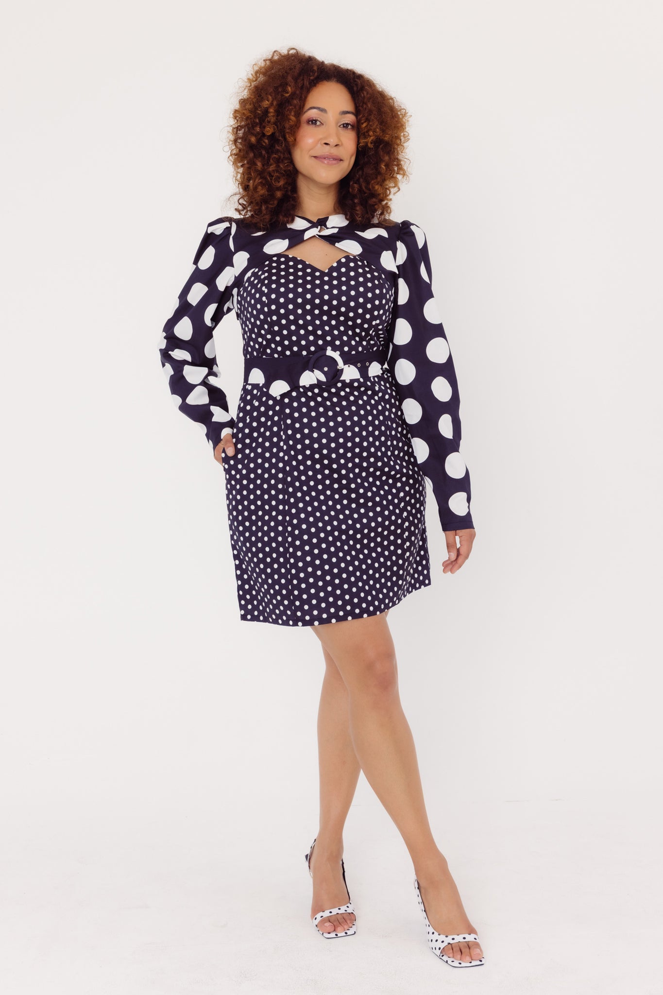 Front view of a woman wearing a Cherry Bobbins black polka dot dress with long sleeves on a white background