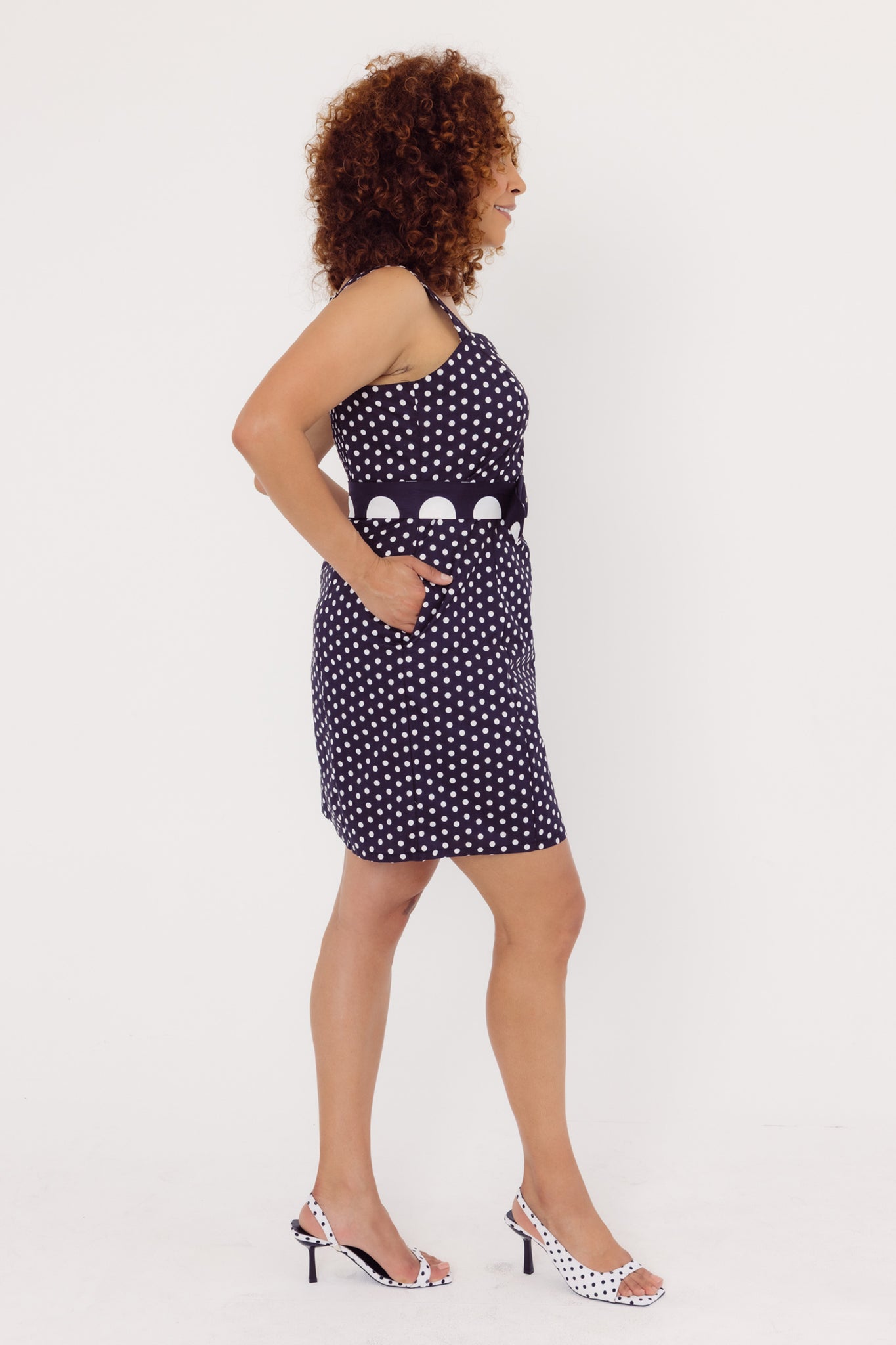 Side view of a woman wearing a black Cherry Bobbins Polka Dot dress on a white background
