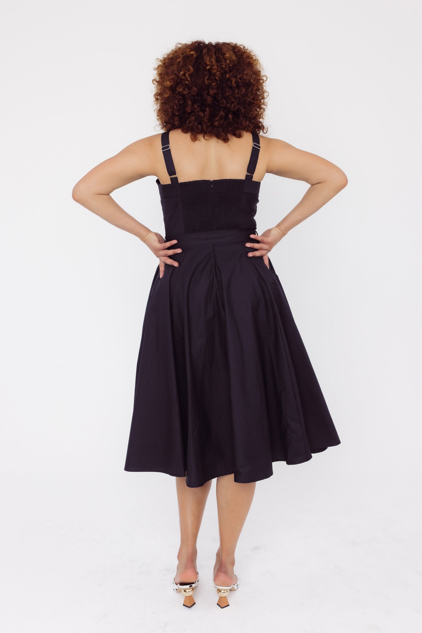 Back view of a woman wearing a Cherry Bobbins plain black dress with a elasticated back bodice and self covered belt