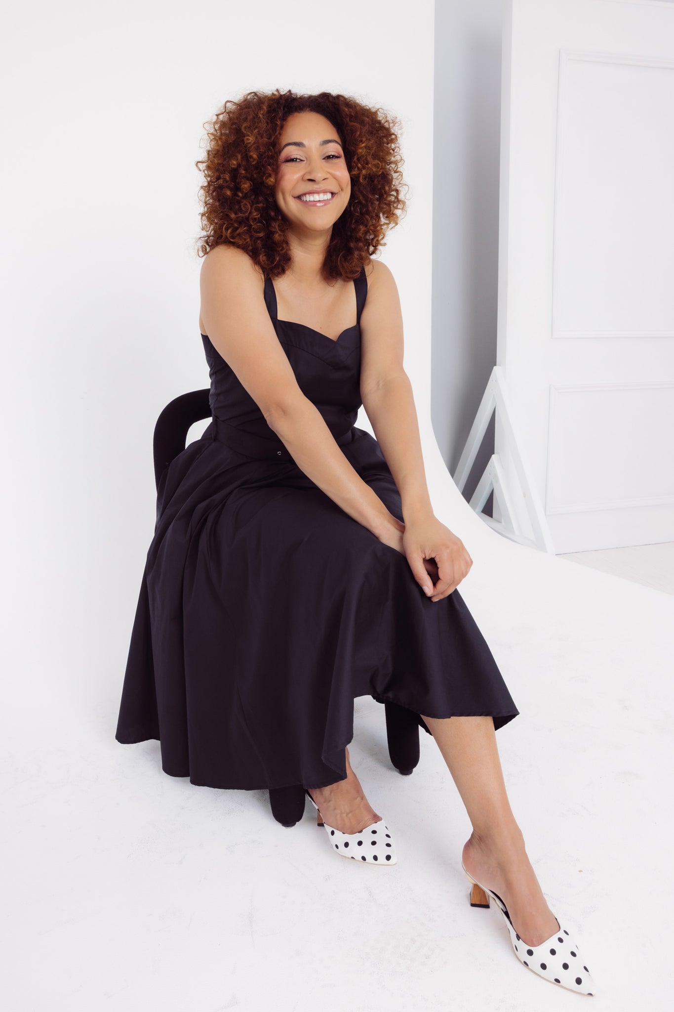 Woman sitting on a black chair in a Cherry Bobbins plain cotton black dress 