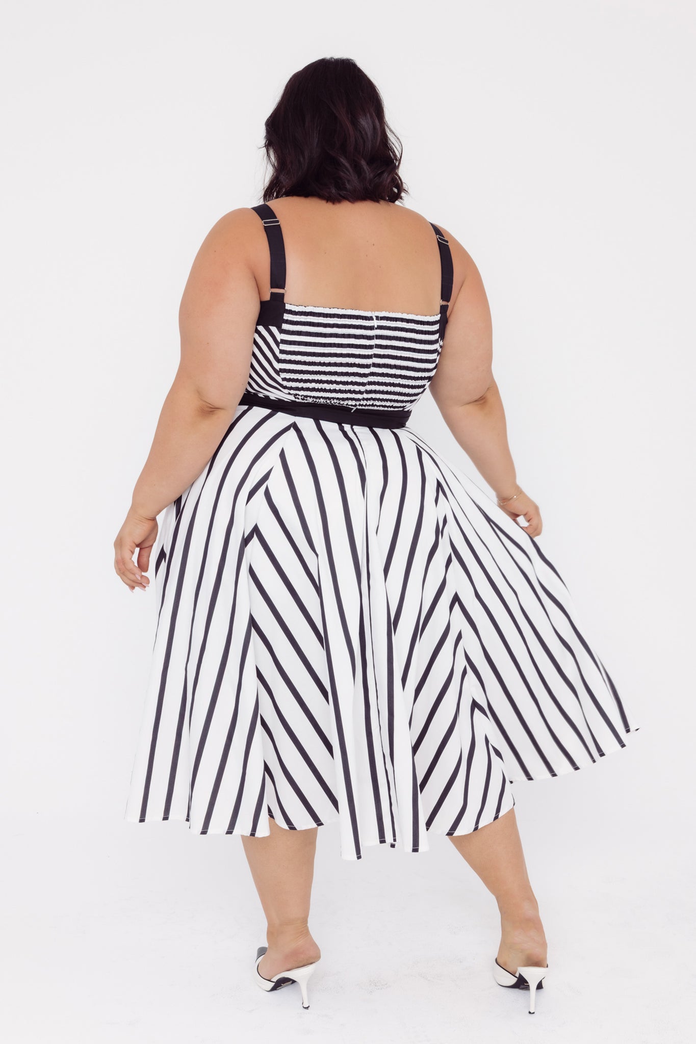 Back view of a woman wearing a Cherry Bobbins black and white striped cotton midi dress on a white background