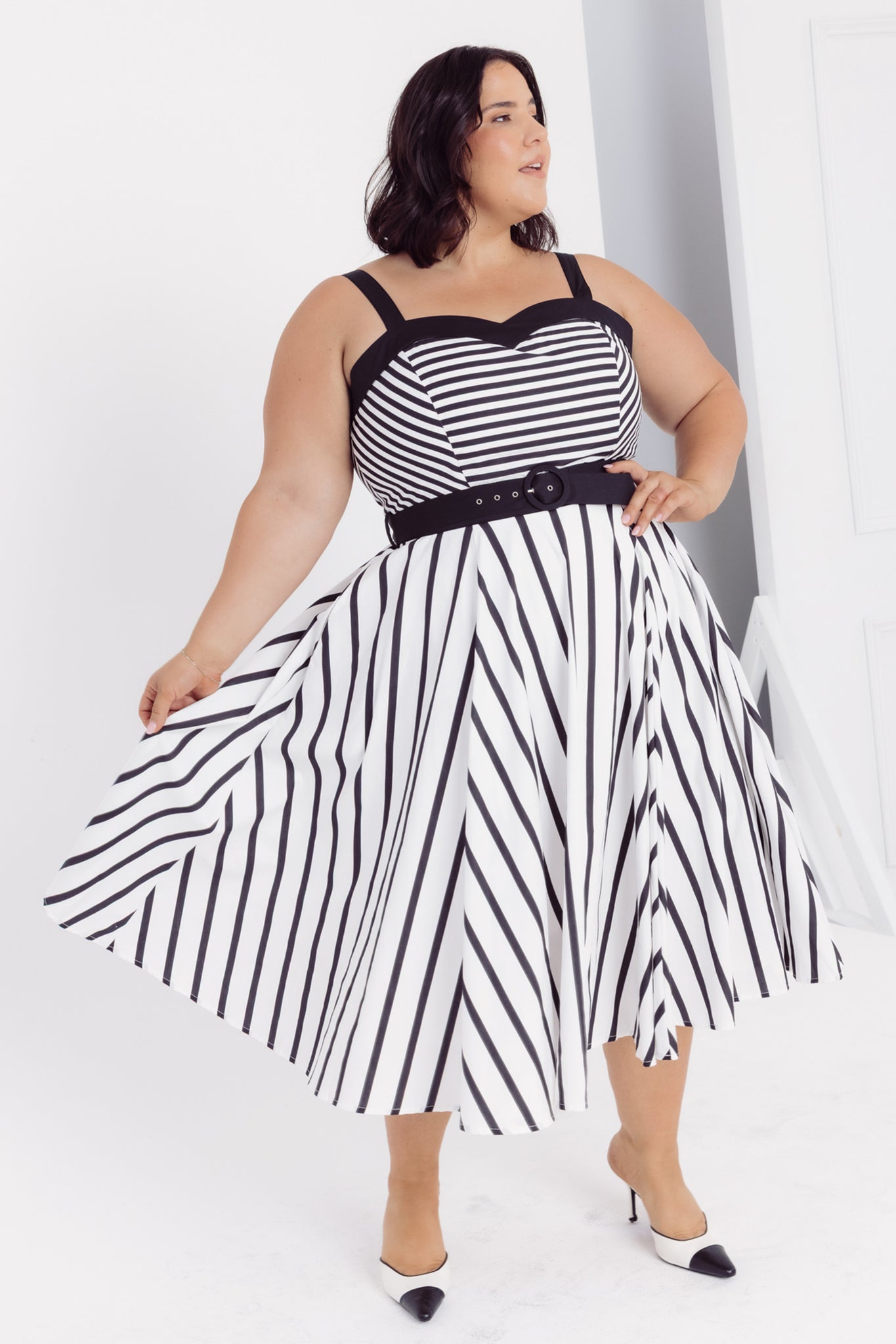 Close up view of a woman wearing a Cherry Bobbins black and white striped cotton midi dress with a belt on a white background