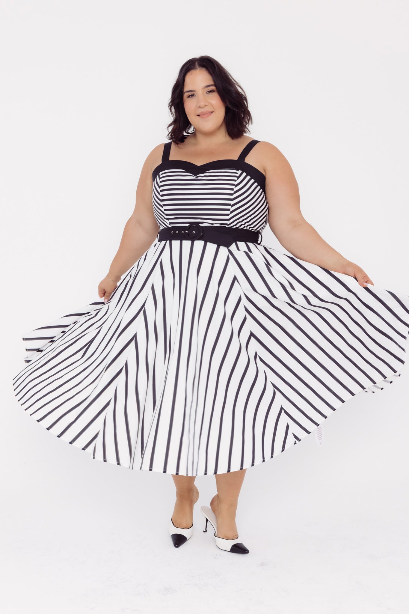 Front view of a woman wearing a Cherry Bobbins black and white striped midi cotton dress twirling on a white background