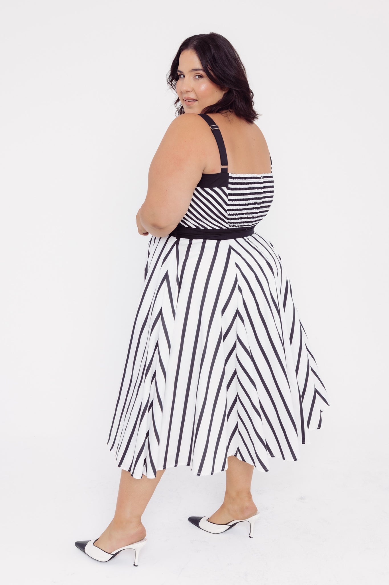 Side view of a woman wearing a Cherry Bobbins black and white striped midi cotton dress on a white background