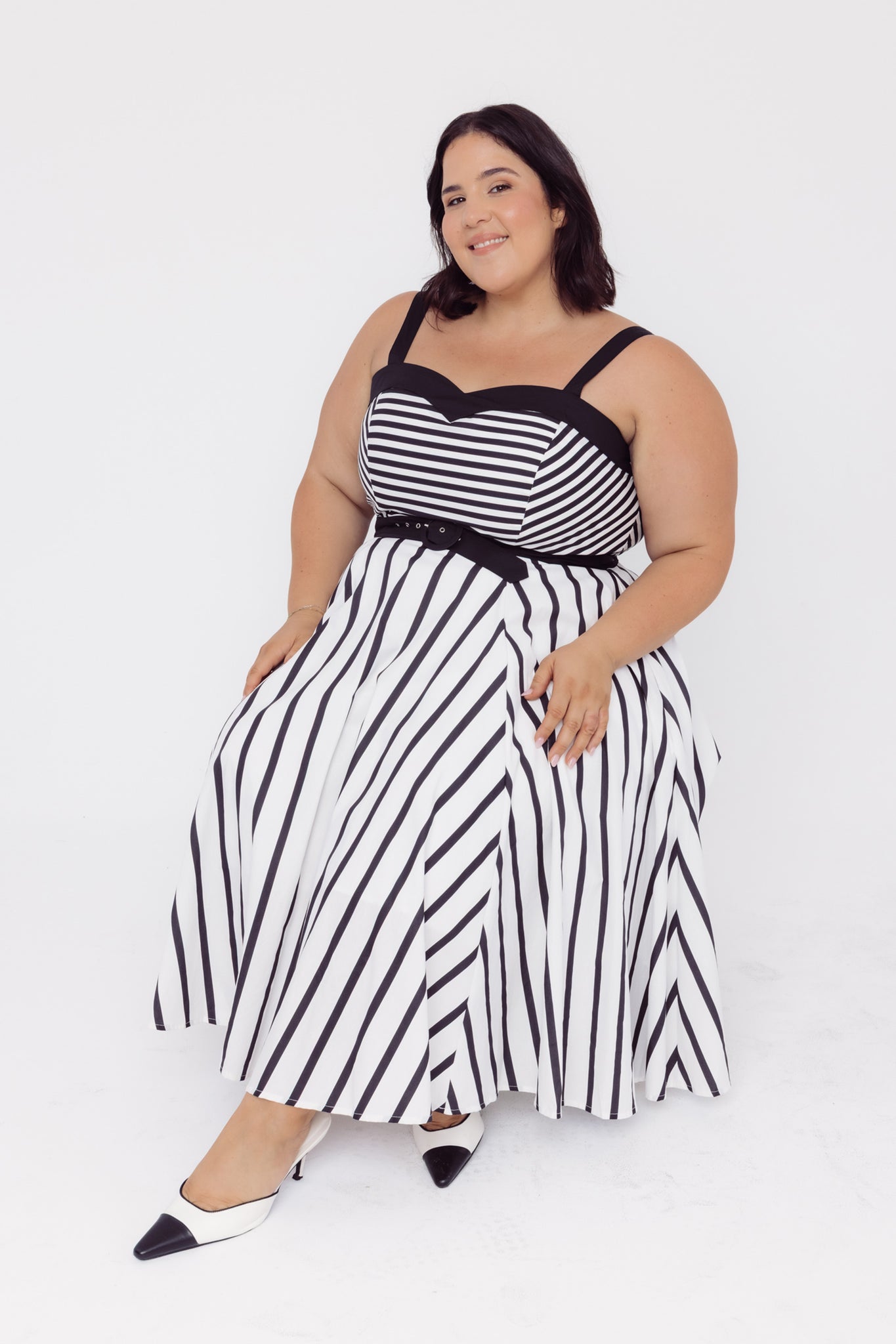 Woman wearing a Cherry Bobbins black and white striped cotton midi dress, while sitting on a white background