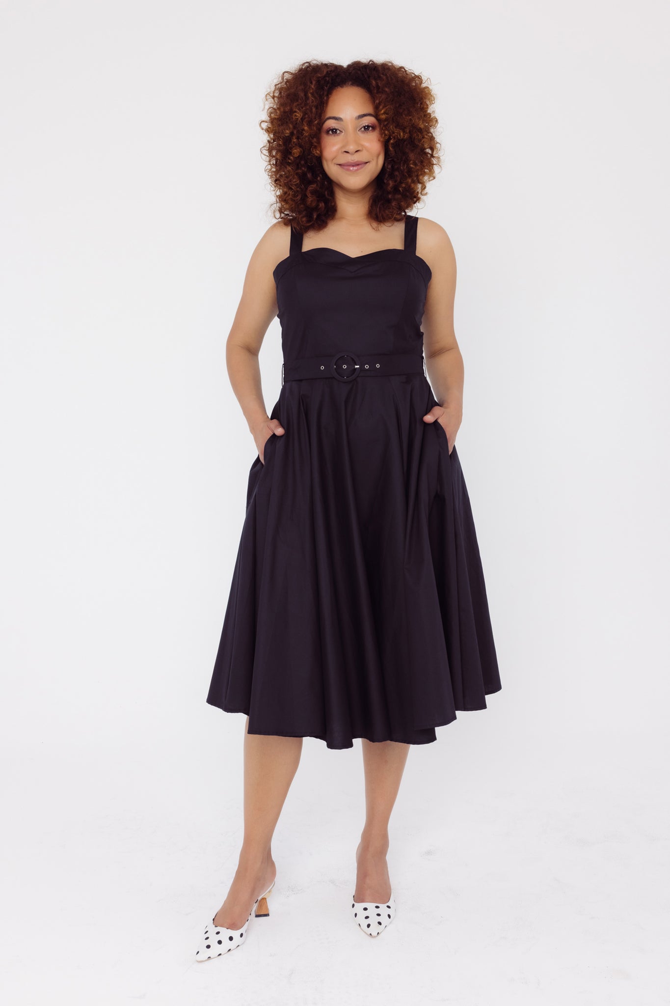 Front view of a woman wearing a Cherry Bobbins plain cotton black dress with a white background