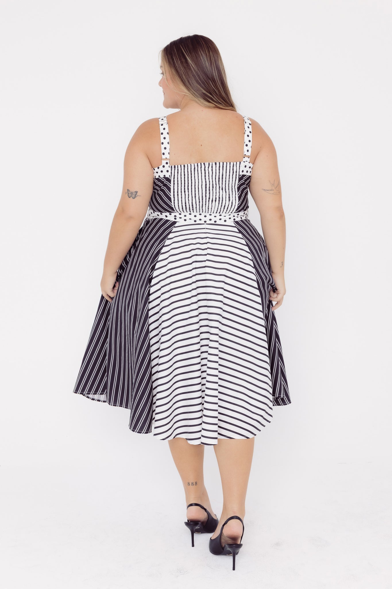 Back view of a mid-sized woman wearing a Cherry Bobbins black and white striped cotton midi dress with a polka dot waistband 