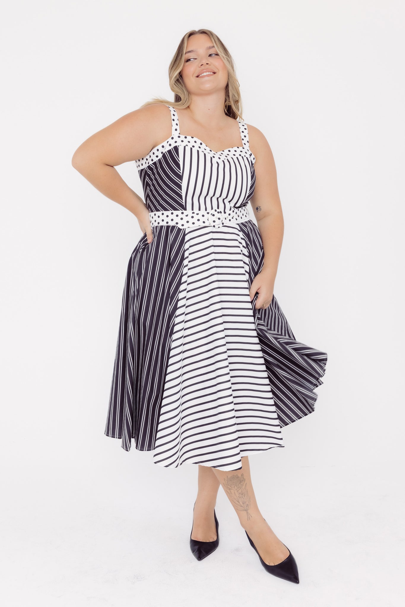 Front view of a mid-sized woman wearing a black and white striped cotton midid dress with a polka dot belt