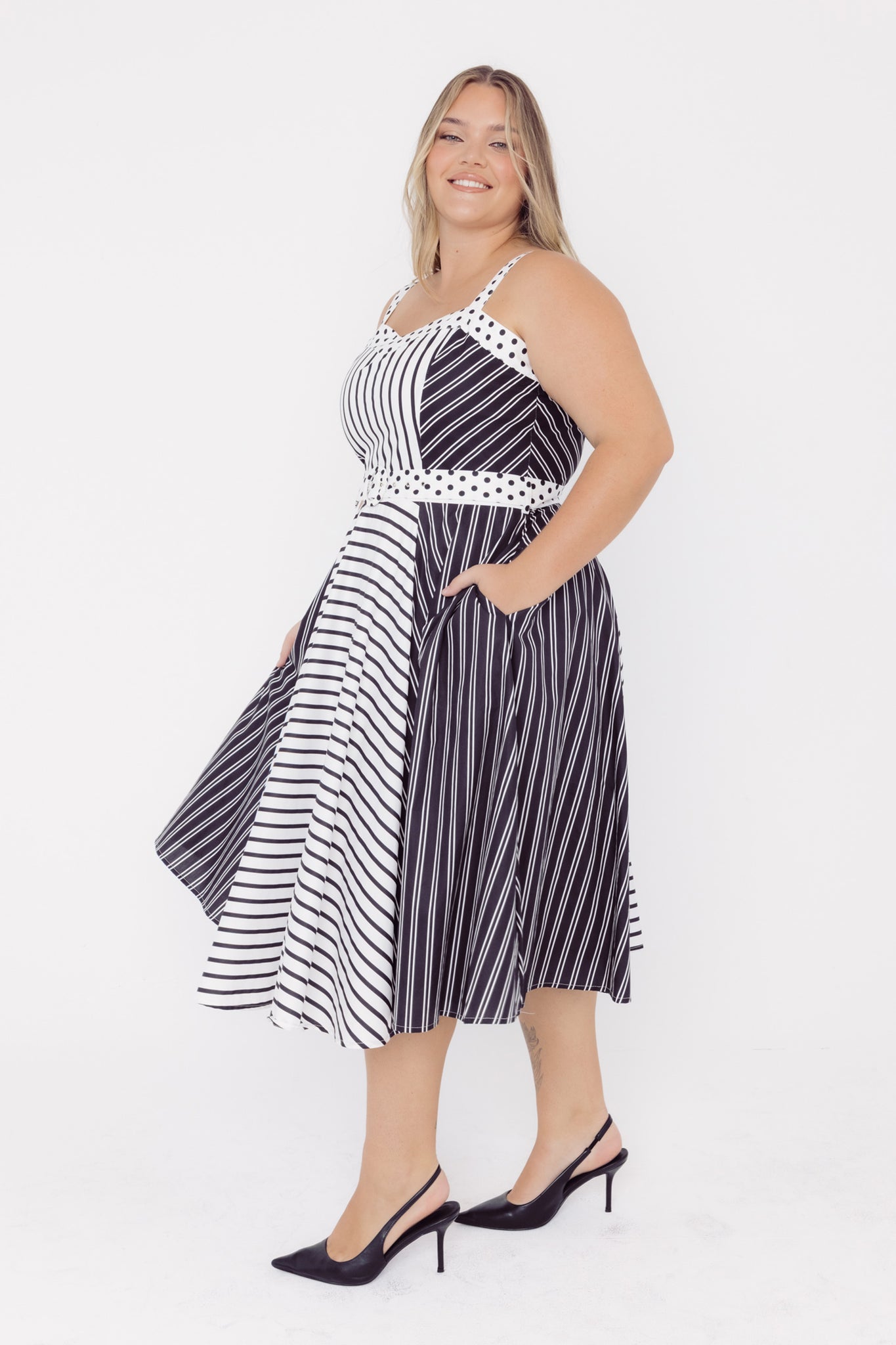 Side view of a mid-sized woman wearing a black and white striped dress with a polka dot belt on a white background