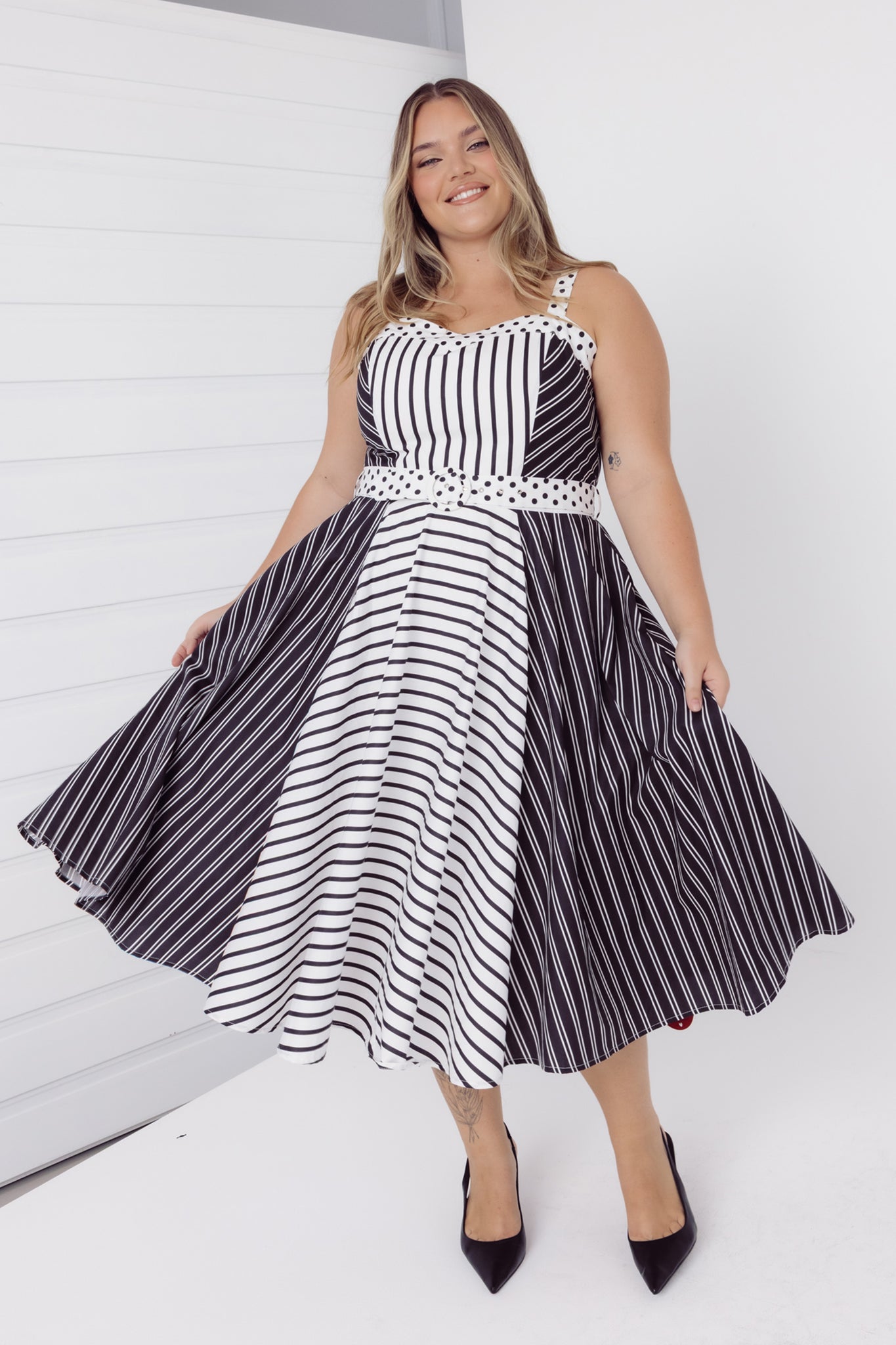 Front view of a woman swinging her skirt of a Cherry Bobbins black and white striped midi cotton dress
