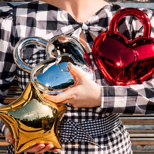 Person holding three metallic heart and star shaped reflective bags in red, gold, and silver.