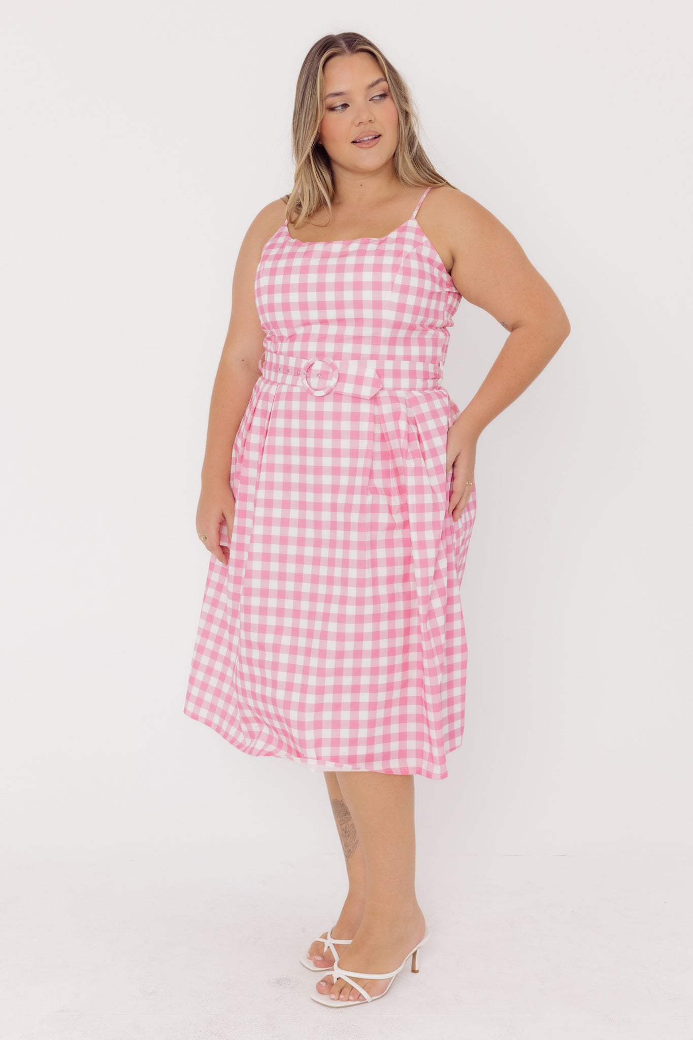 Front view of a woman wearing a pCherry Bobbins pink gingham sustainable cotton dress on a white background