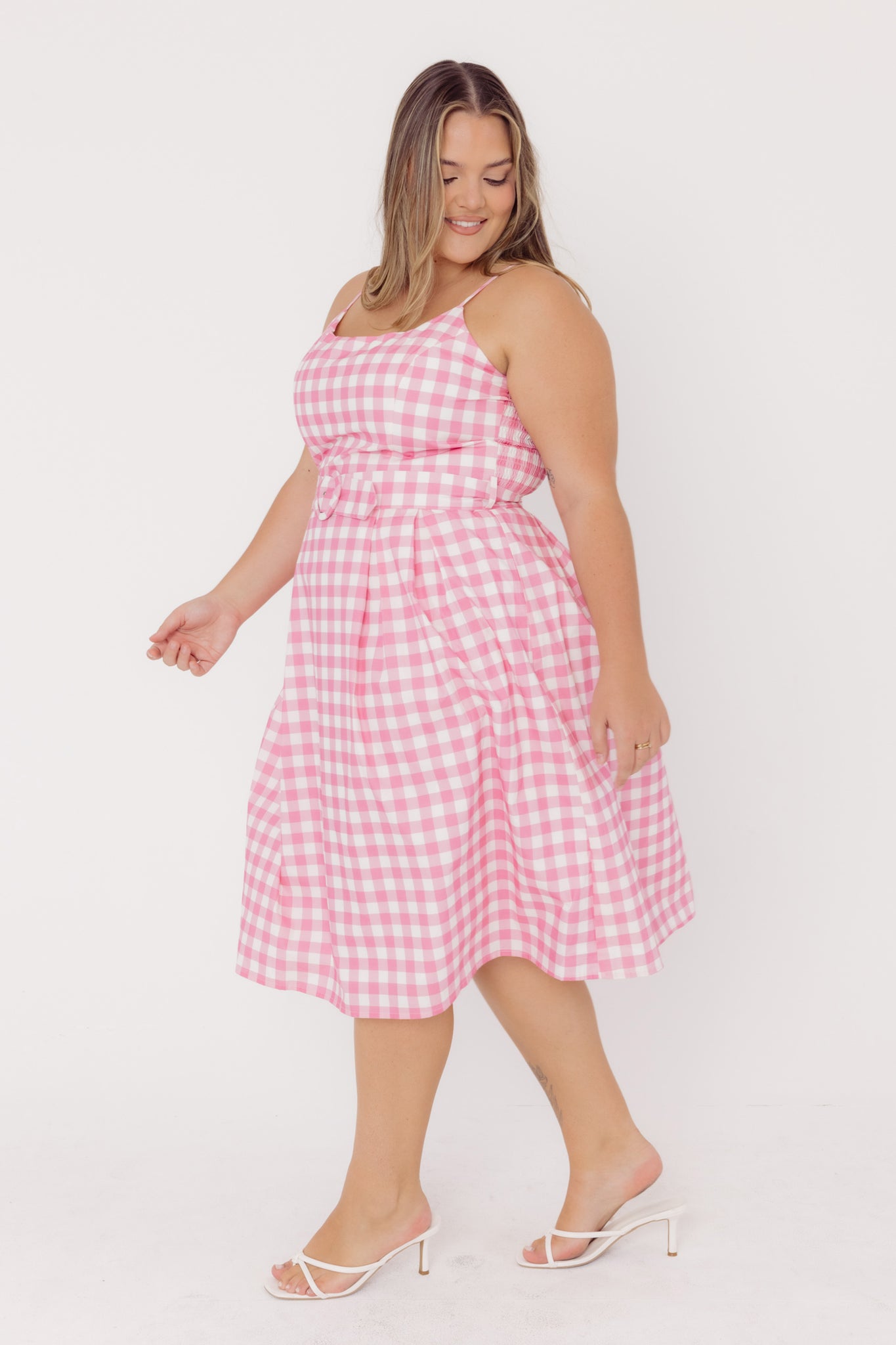 Side view of a woman wearing a Cherry Bobbins sustainable cotton pink gingham dress on a white background