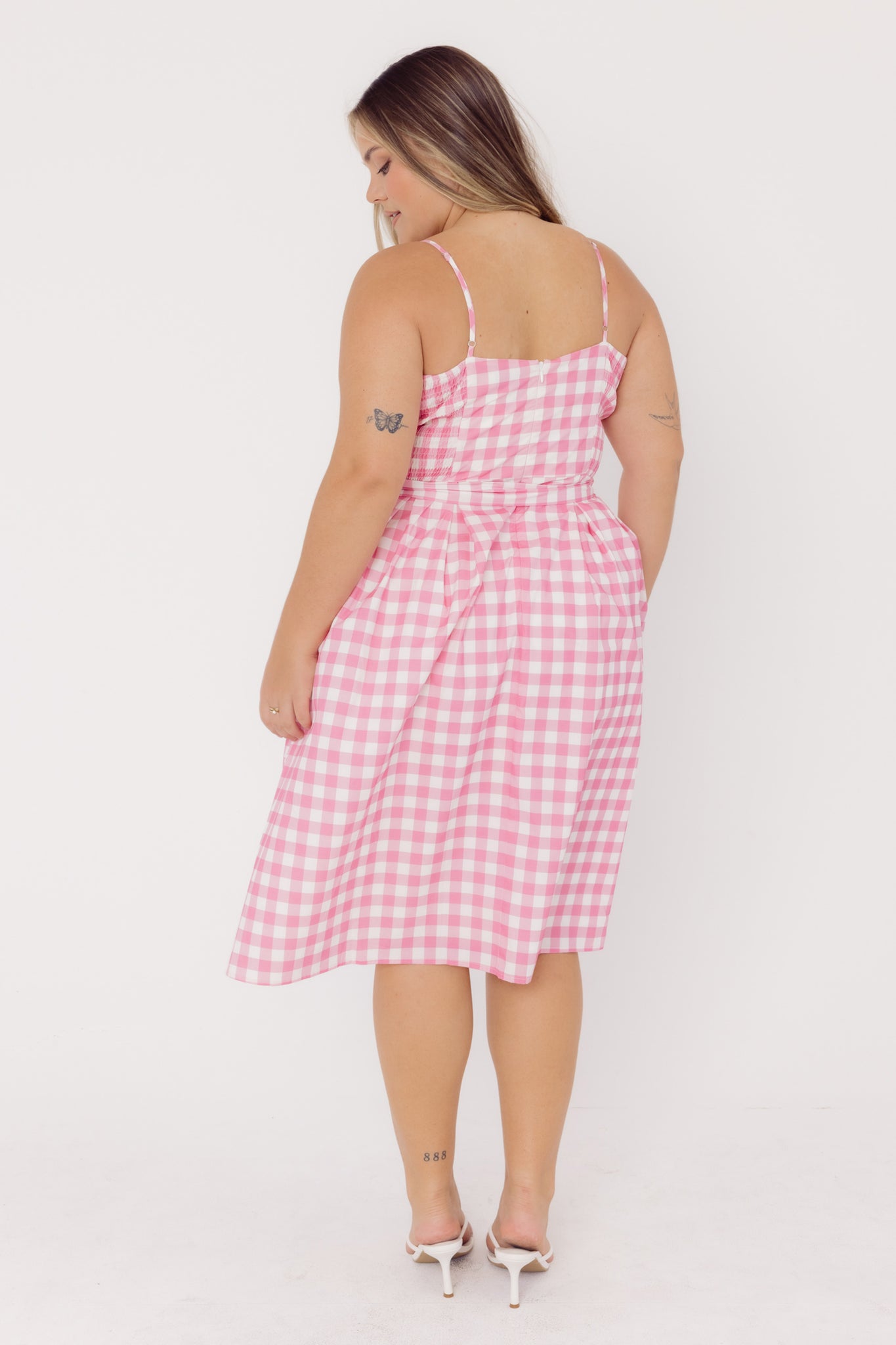Back View of a woman wearing a Cherry Bobbins pink gingham dress against a white background