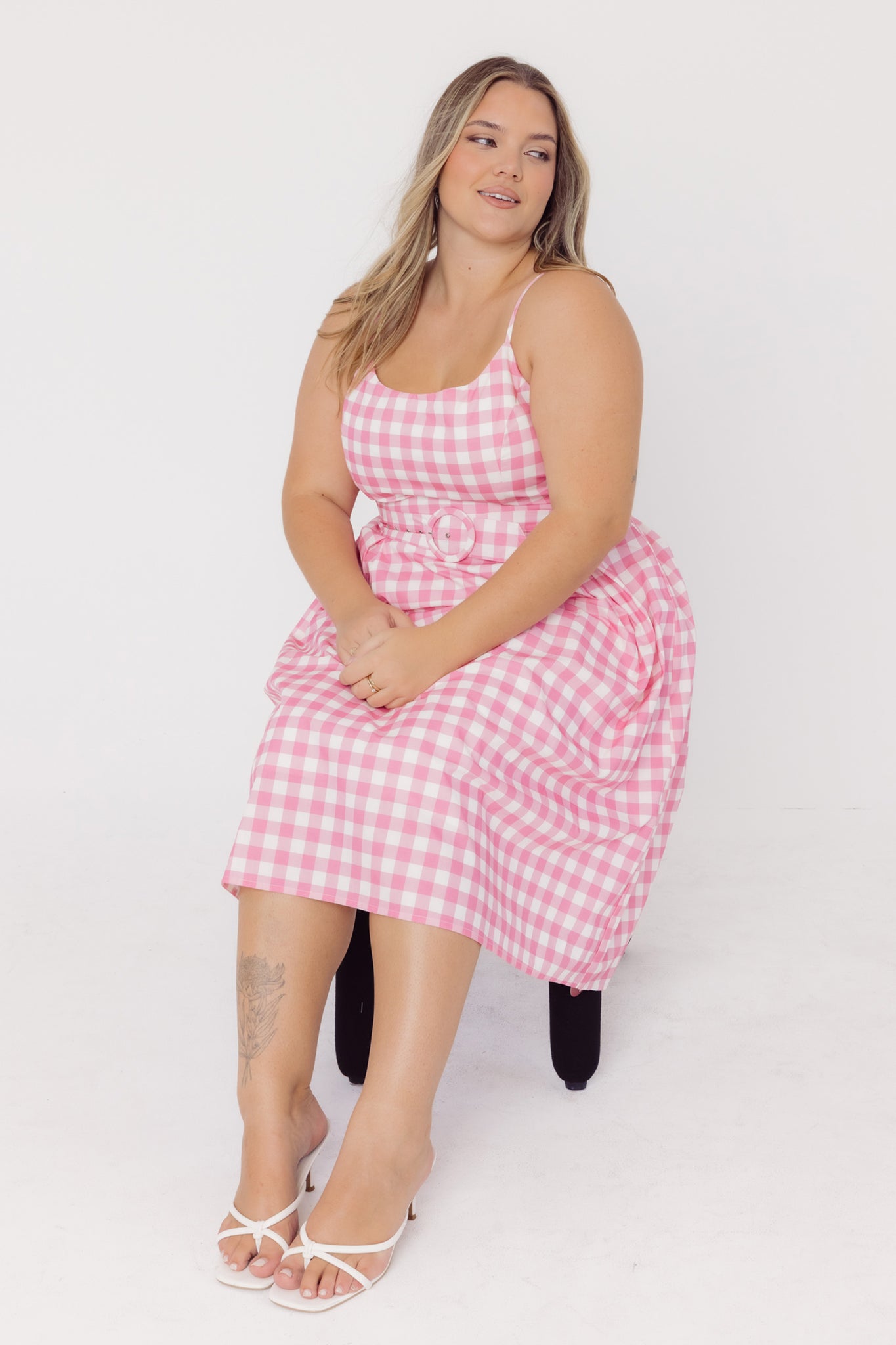 Woman wearing a Cherry Bobbins pink gingham cotton midi dress while sitting on a chair