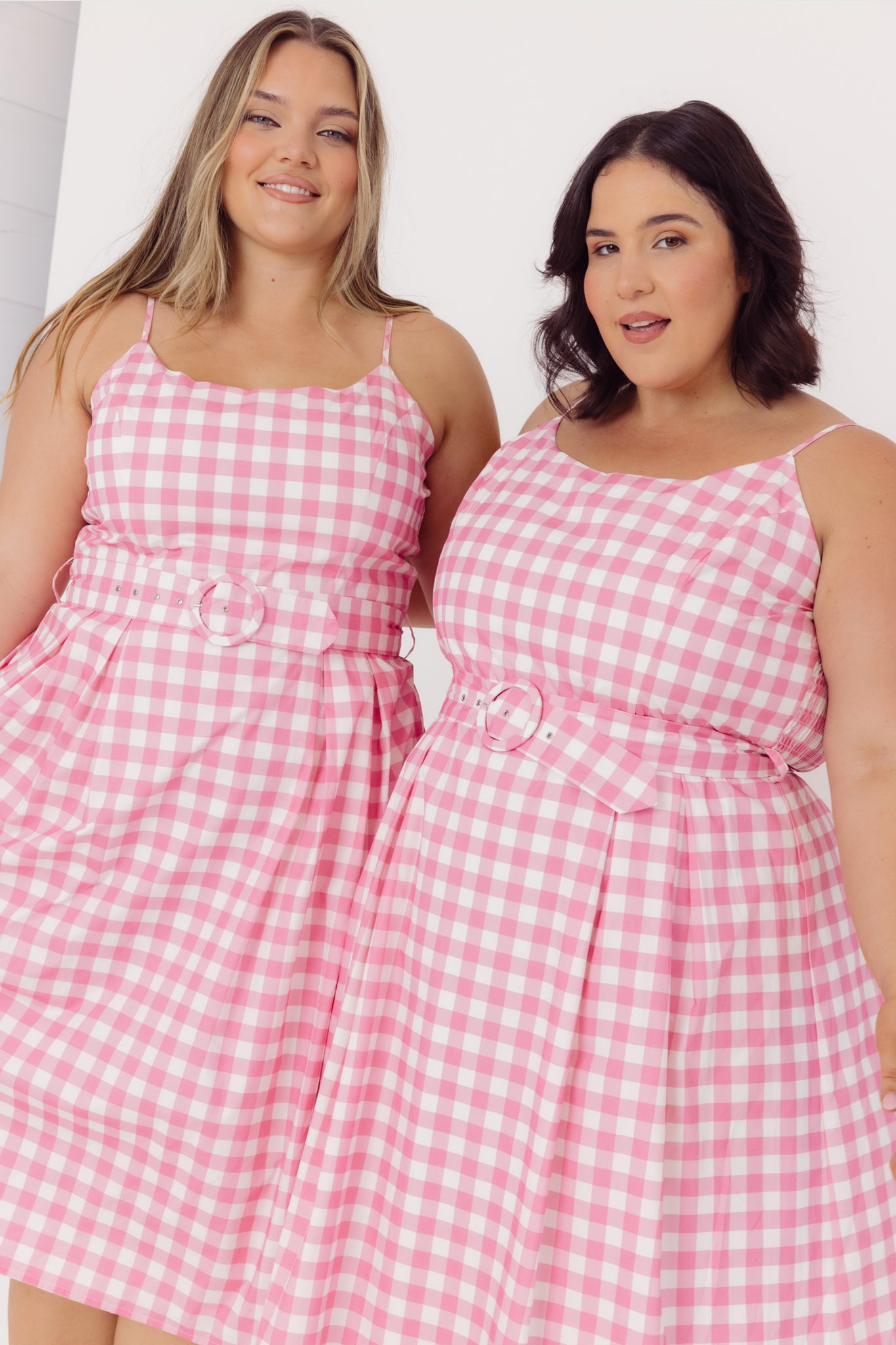 Two women wearing Cherry bobbins Sustainable Cotton pink gingham dresses against a white background